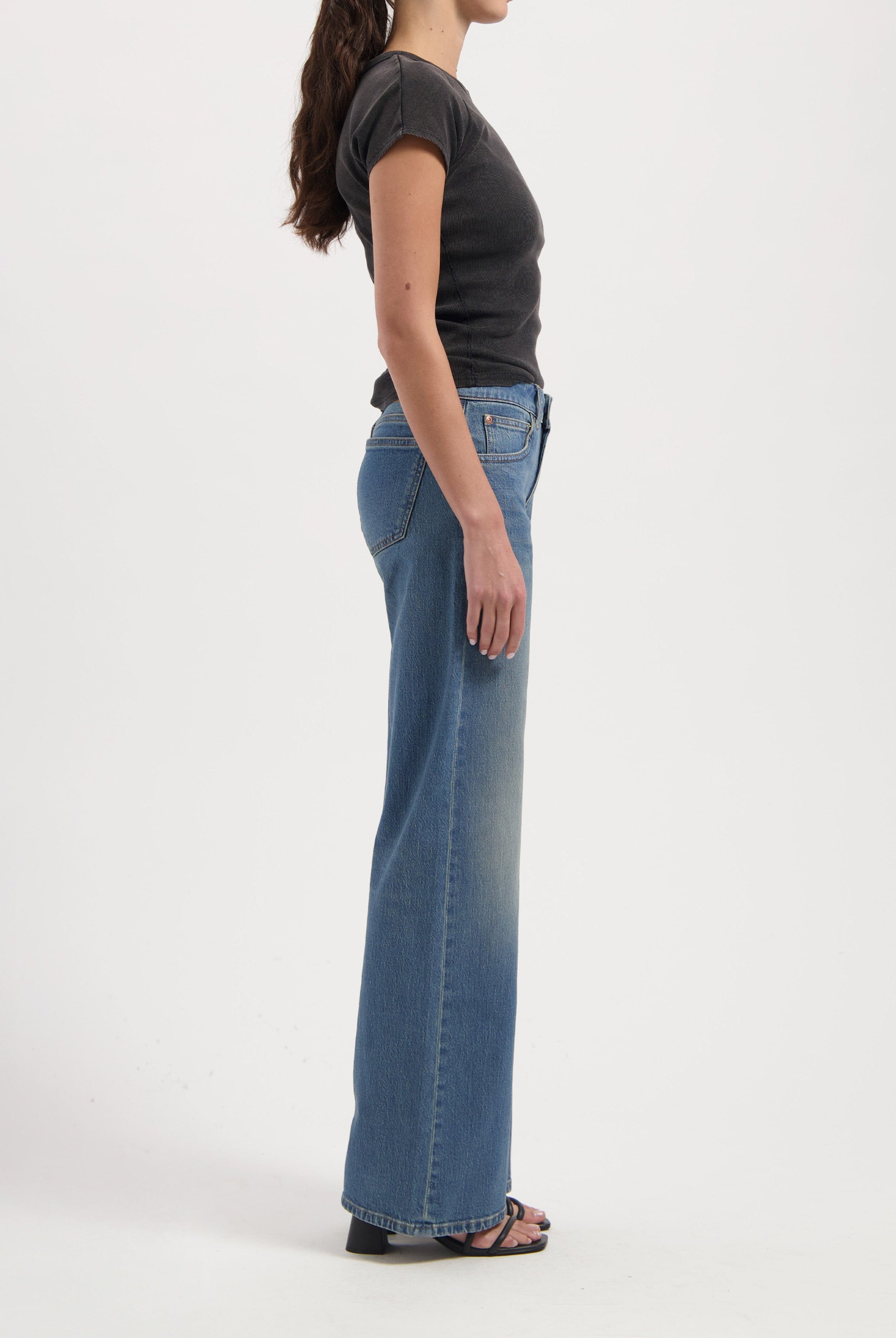 Side view of a woman wearing high-waisted light blue bootcut jeans paired with a fitted black short-sleeve top.