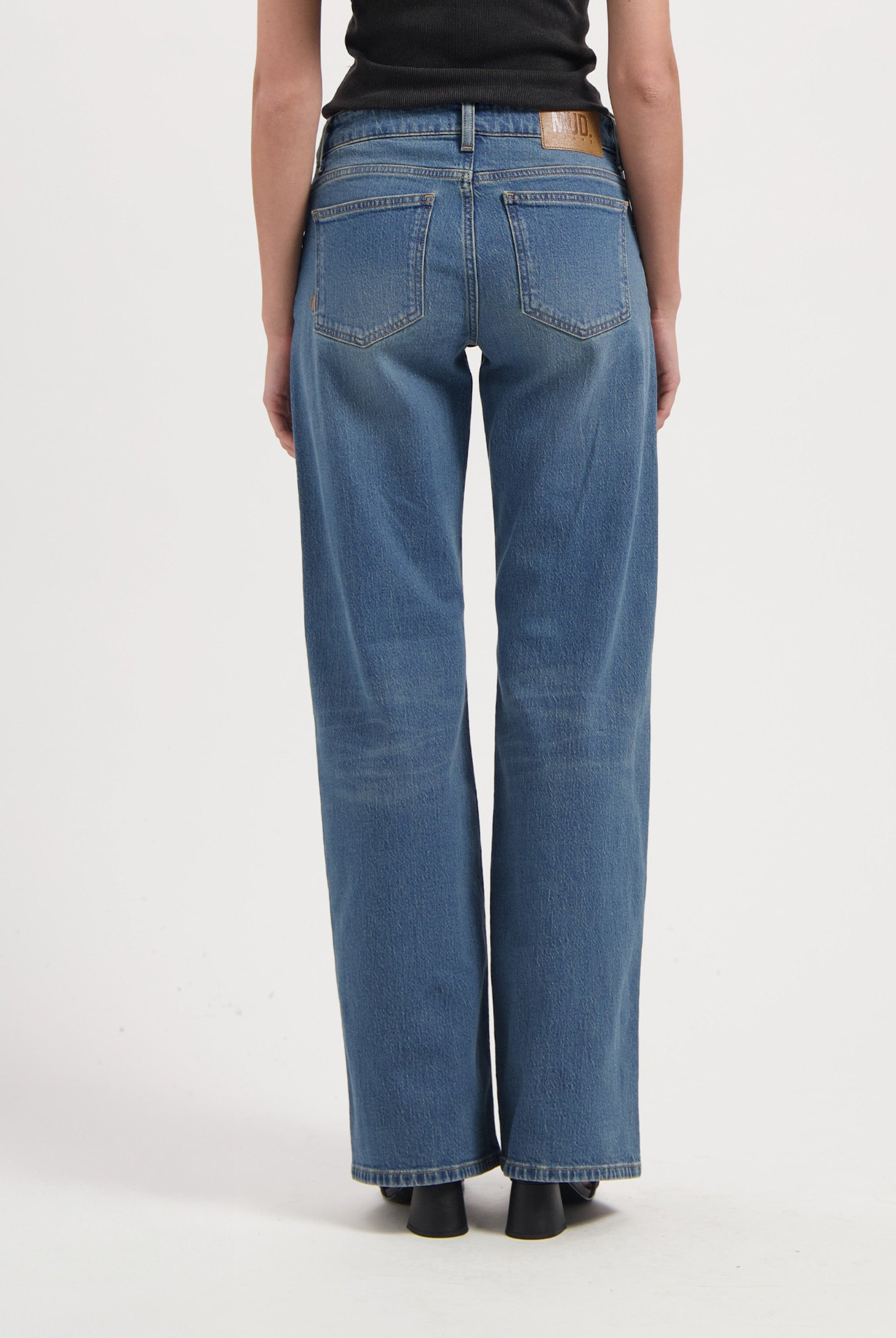 Wide-leg blue jeans made from organic cotton, shown from the back, paired with a black sleeveless top.
