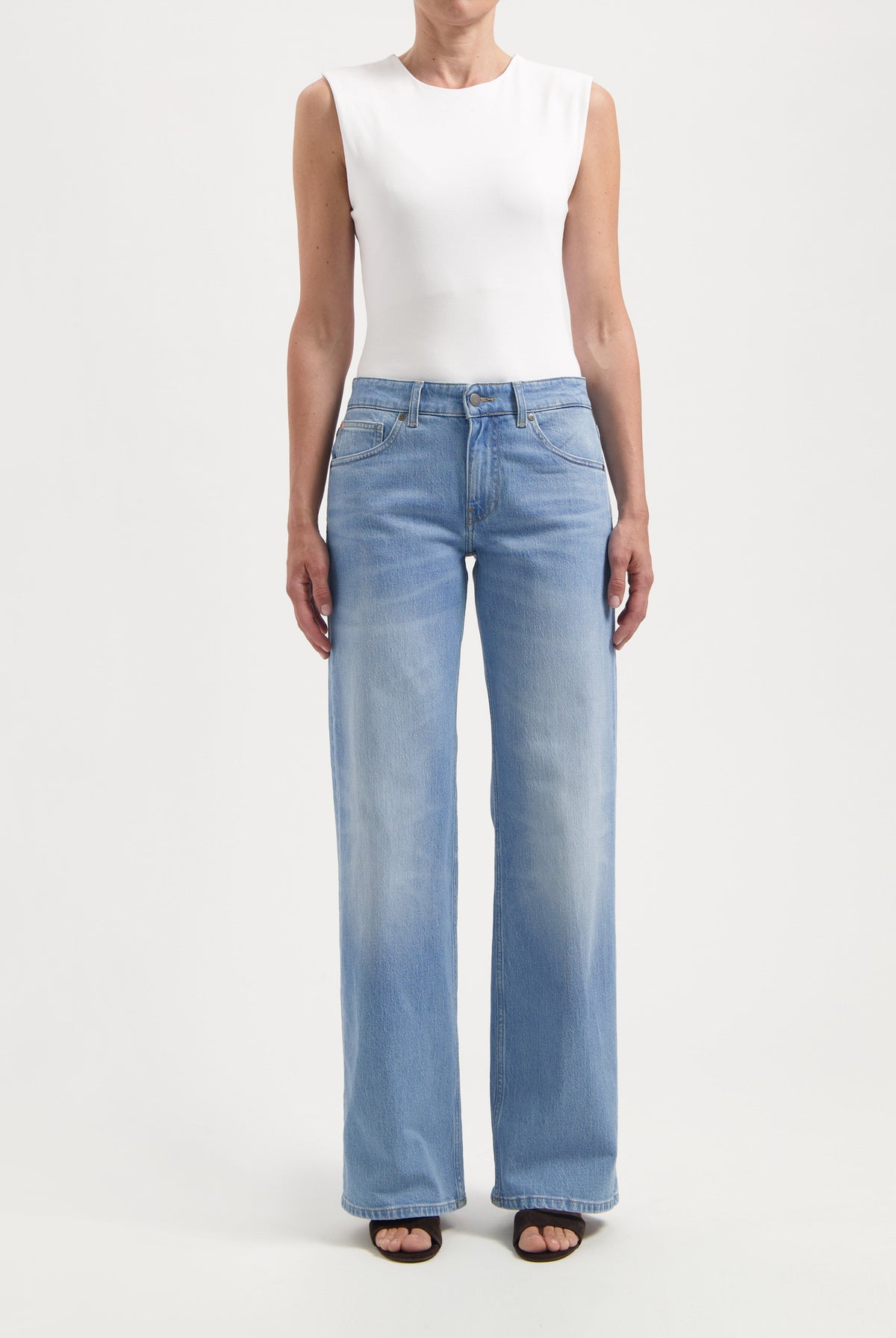 Light blue, high-waisted wide-leg jeans paired with a sleeveless white top worn by a woman standing against a plain backdrop.