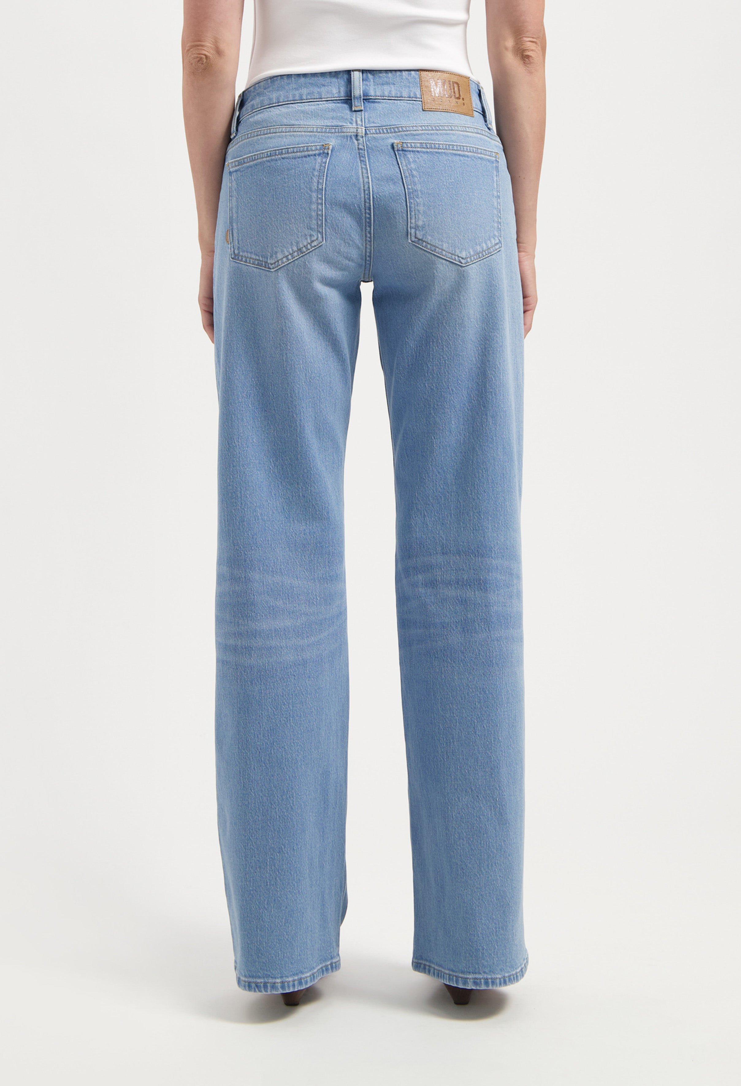Rear view of light blue, straight-leg sustainable jeans made from eco-friendly fabric, worn with a white top.