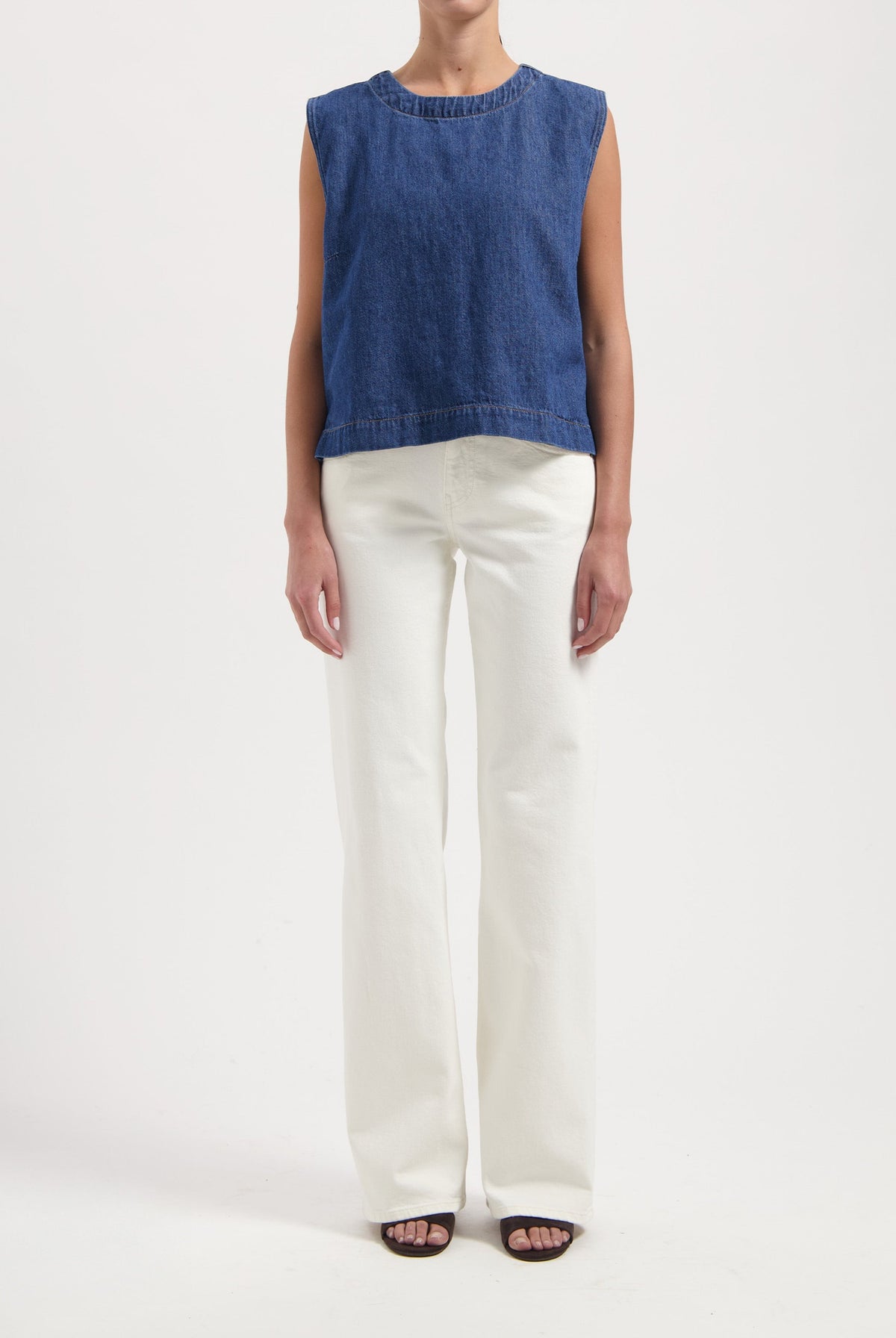 Woman wearing a sleeveless blue denim top paired with high-waisted white wide-leg jeans and black open-toe sandals.