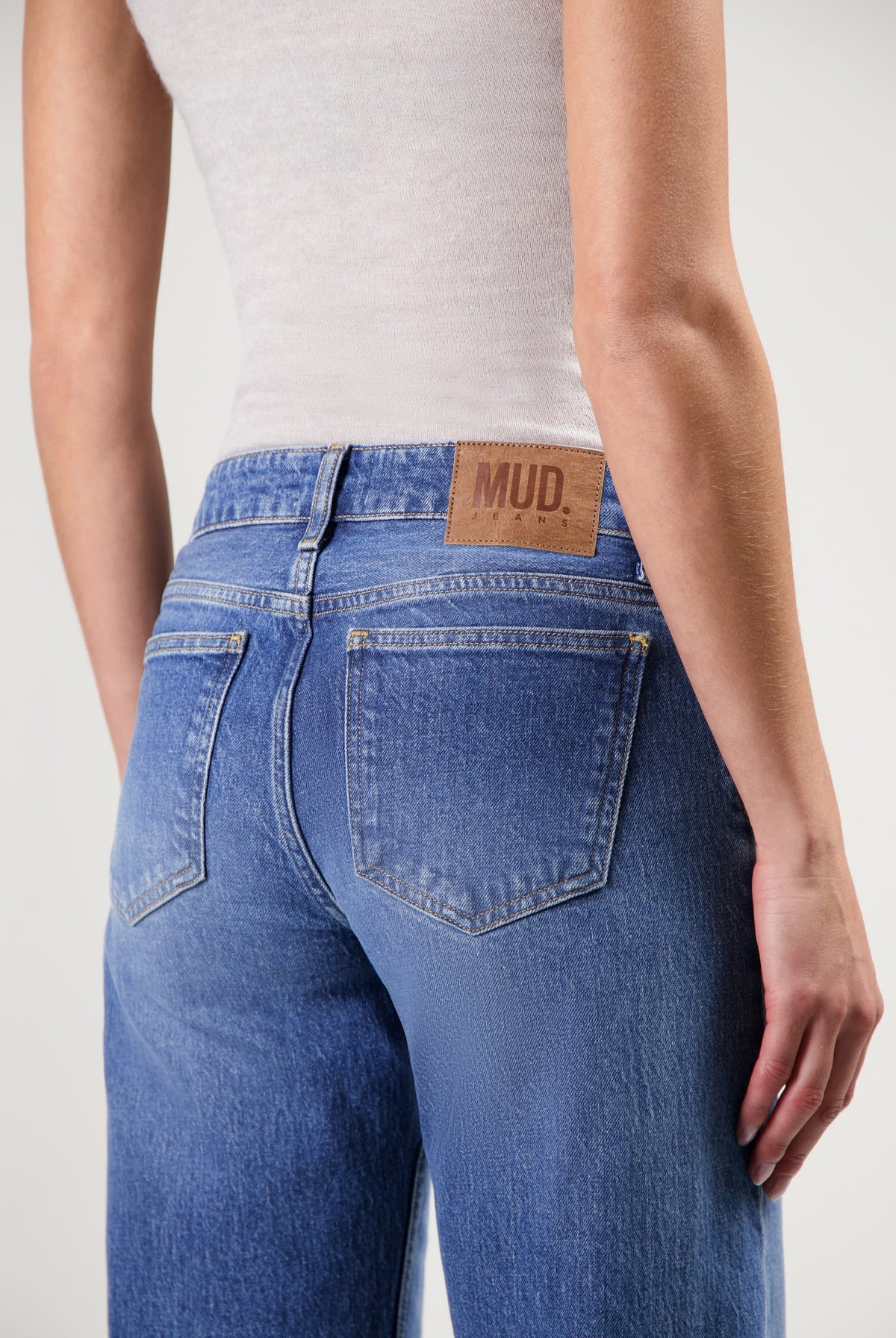 Light blue MUD Jeans from organic cotton, showcasing a close-up of high-rise fit denim worn with a sleeveless white top.