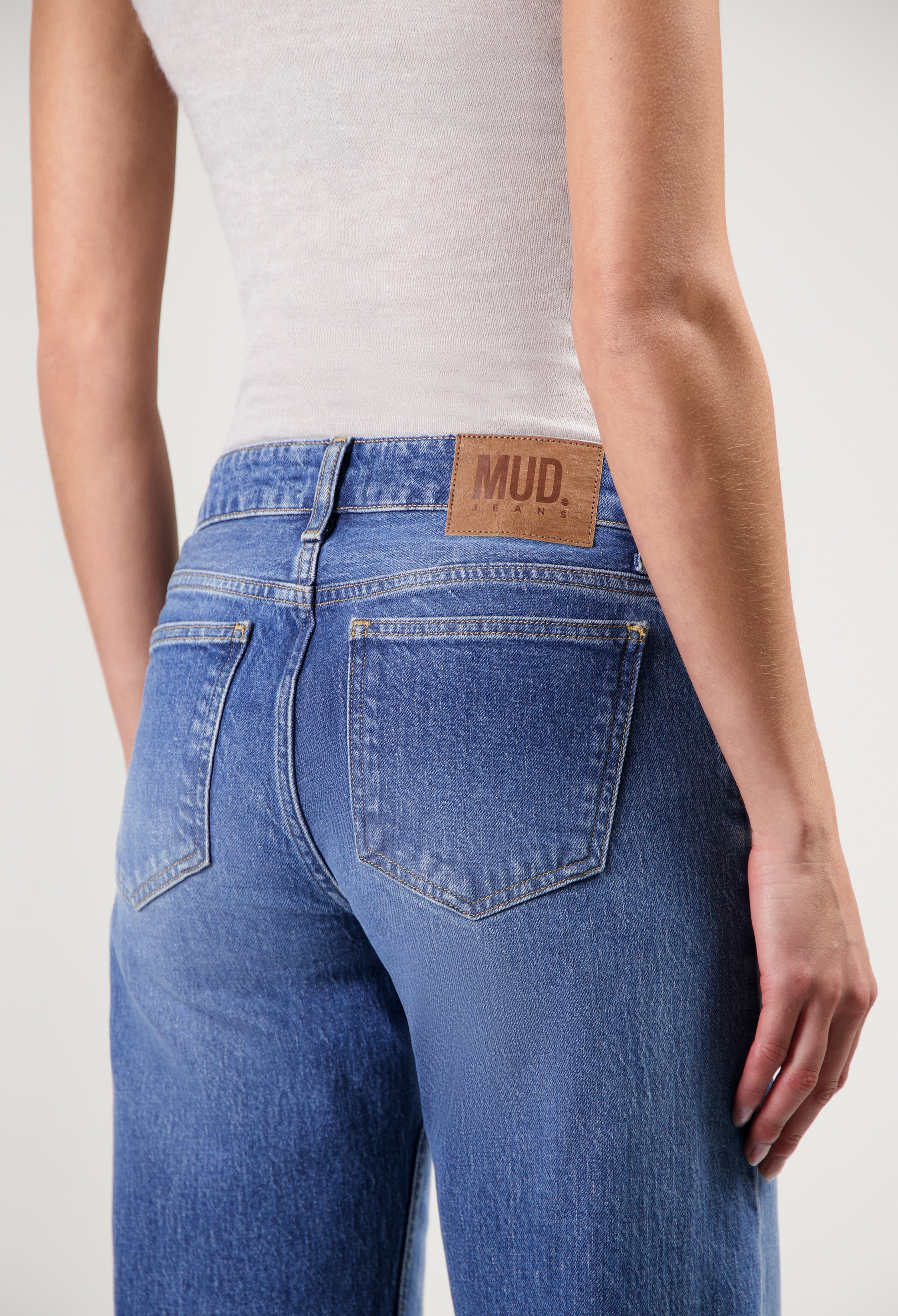 Light blue MUD Jeans from organic cotton, showcasing a close-up of high-rise fit denim worn with a sleeveless white top.