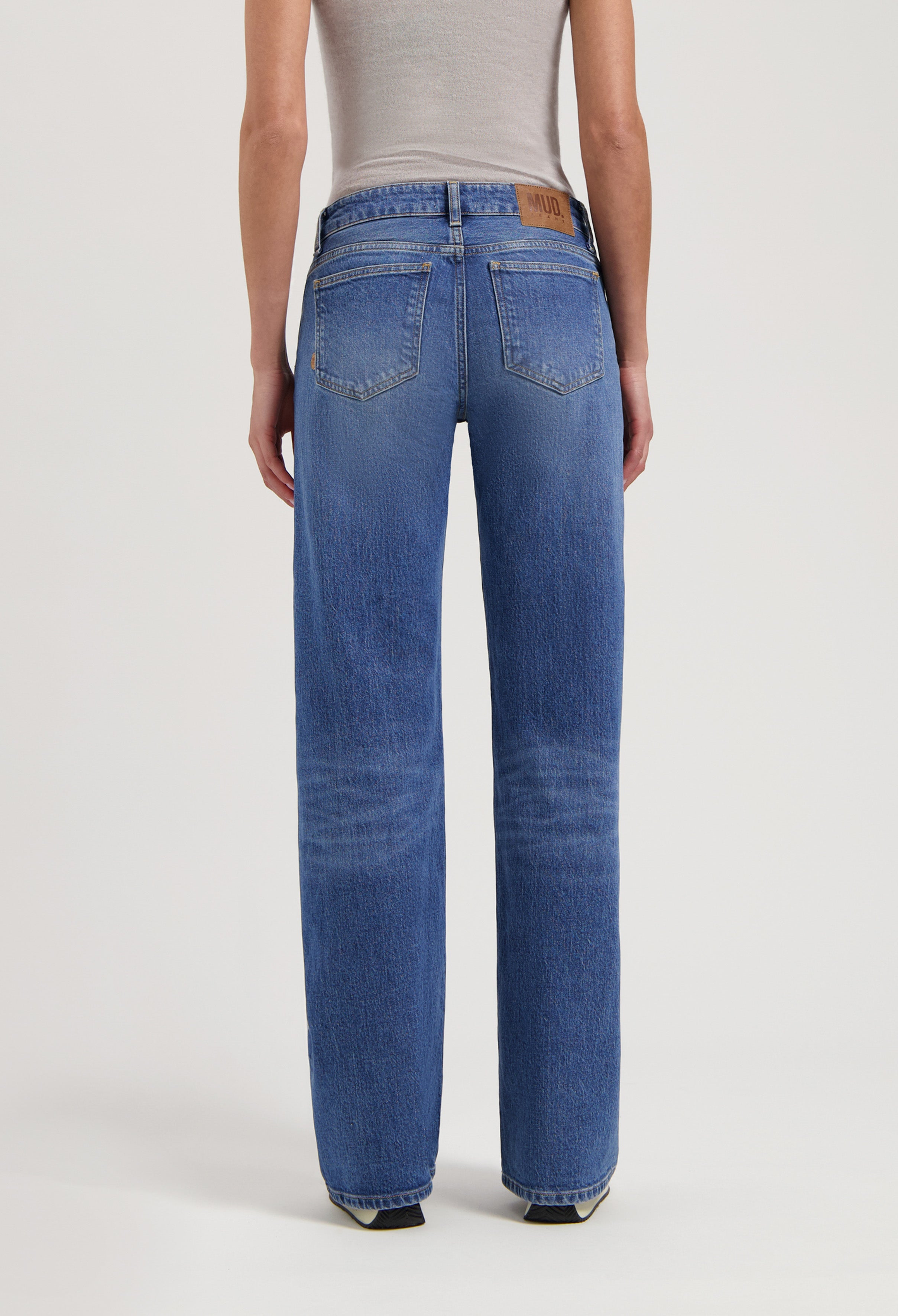 Back view of eco-friendly blue denim jeans by MUD Jeans, featuring a straight-leg fit paired with a beige sleeveless top.