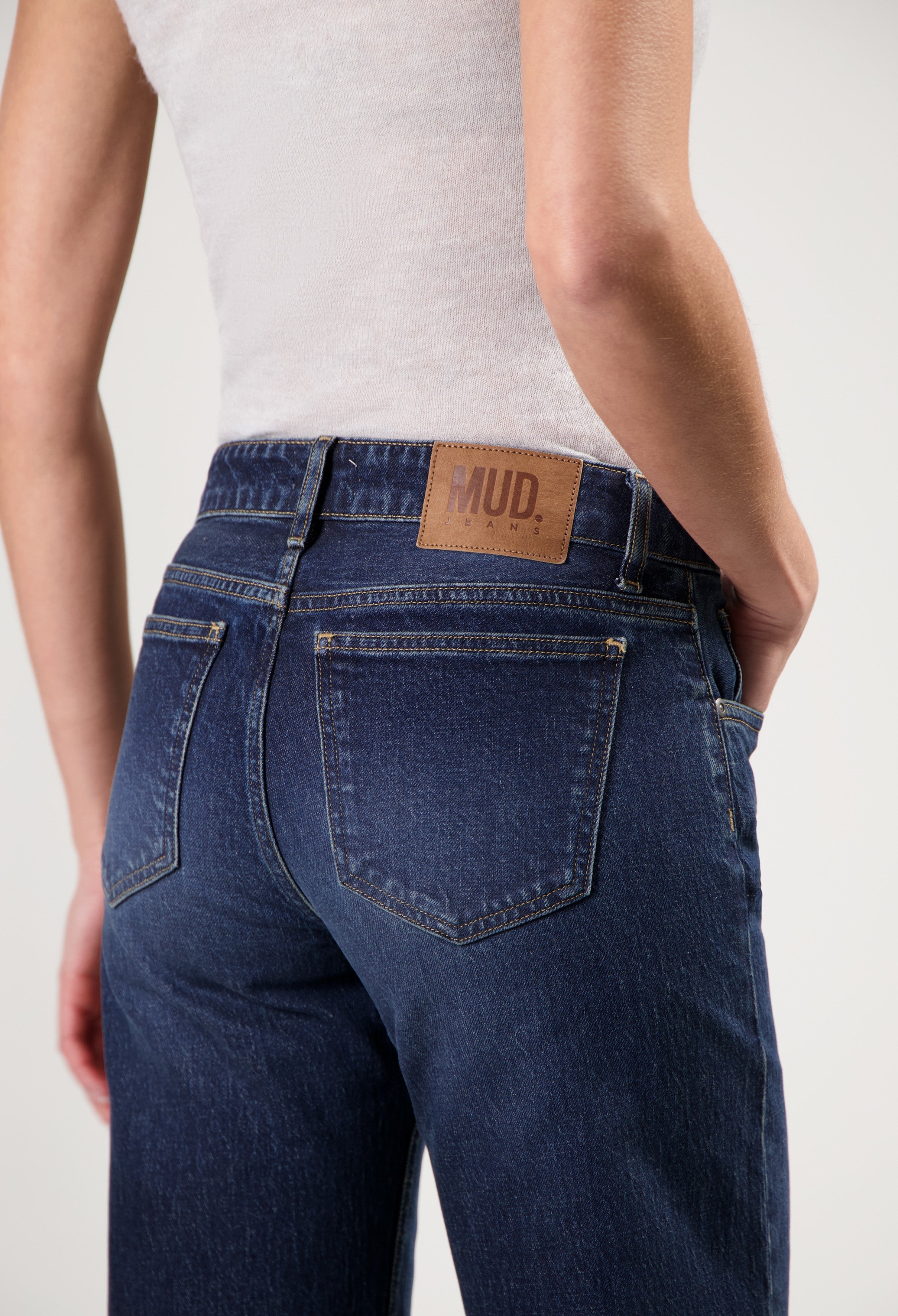 Model wearing dark blue MUD Jeans made from sustainable materials, showcasing slim-fit denim with leather logo patch.