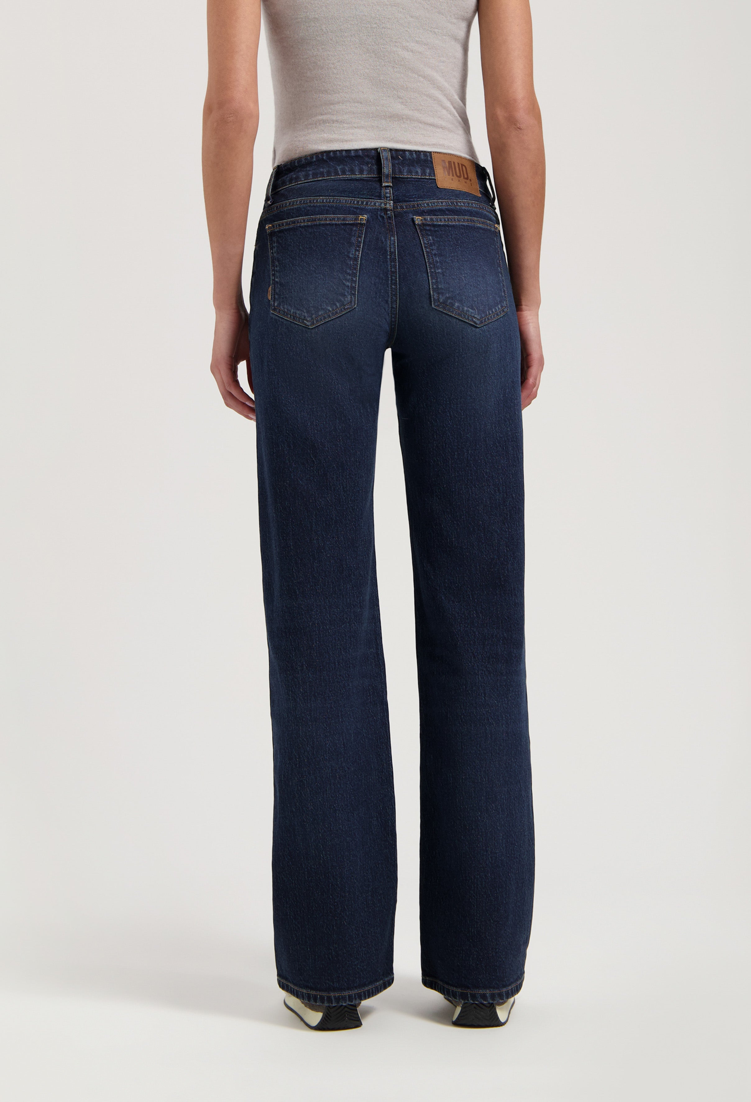 Back view of dark blue sustainable jeans from MUD Jeans, featuring a wide-leg style, paired with a fitted beige tank top.