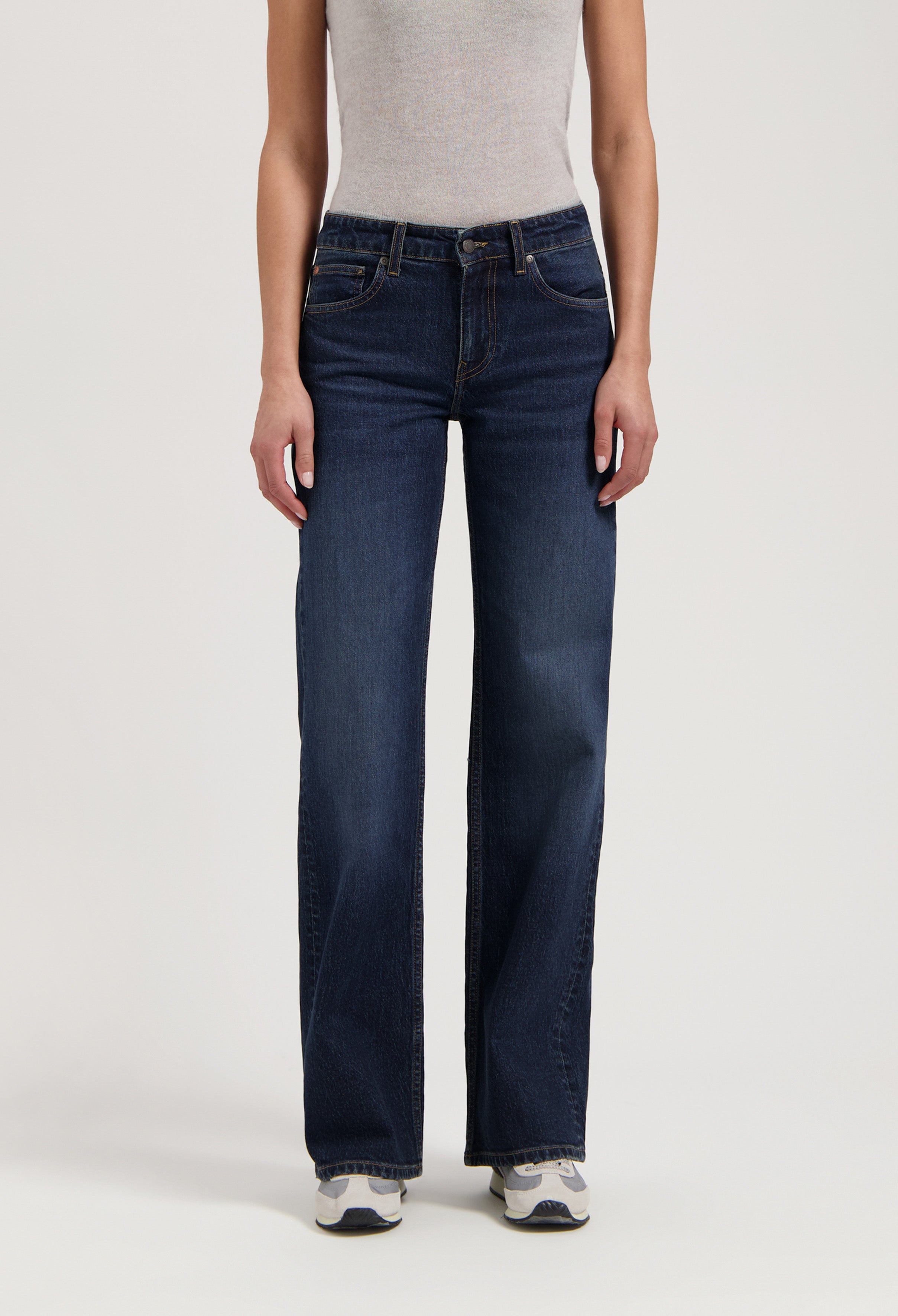 Wide-leg dark blue denim jeans made from organic cotton, worn with a sleek gray sleeveless top and white sneakers.