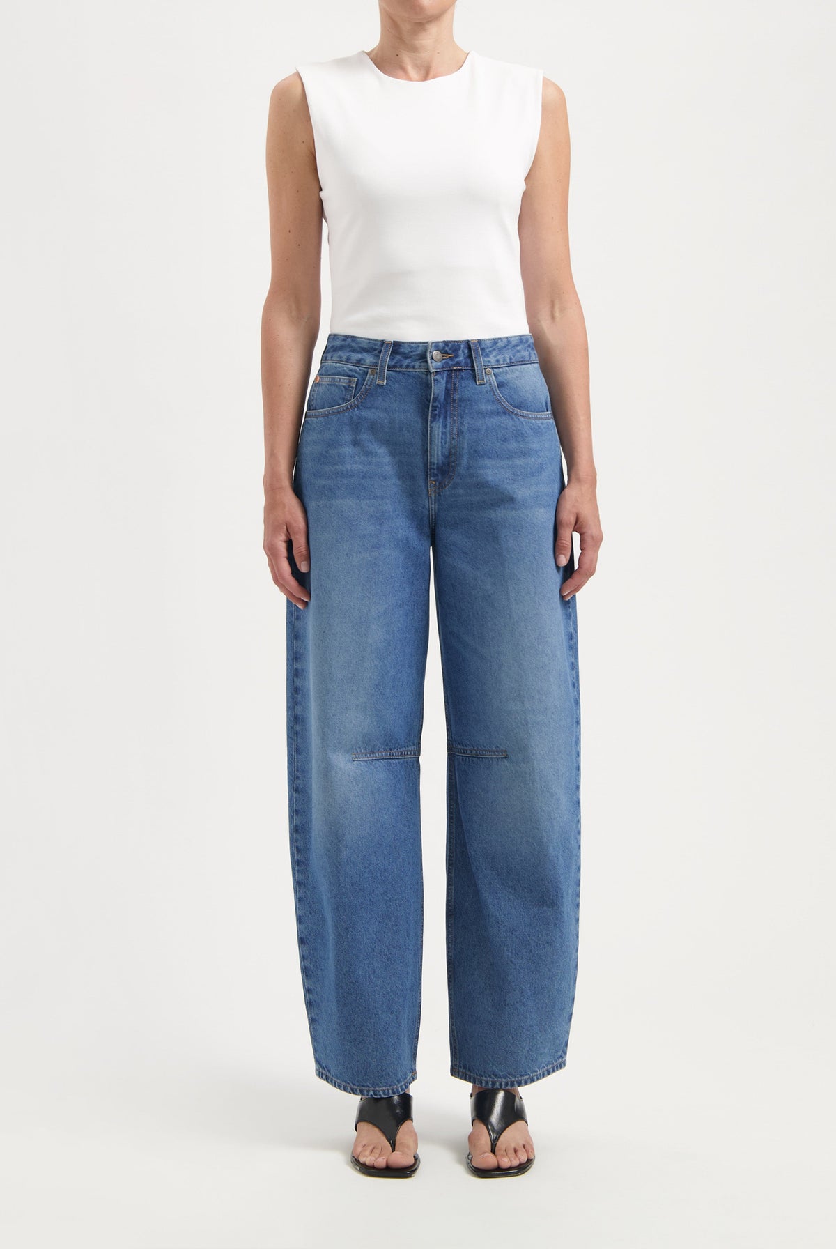 Wide-legged blue denim jeans with pockets and high waist, paired with a sleeveless white top and black sandals.