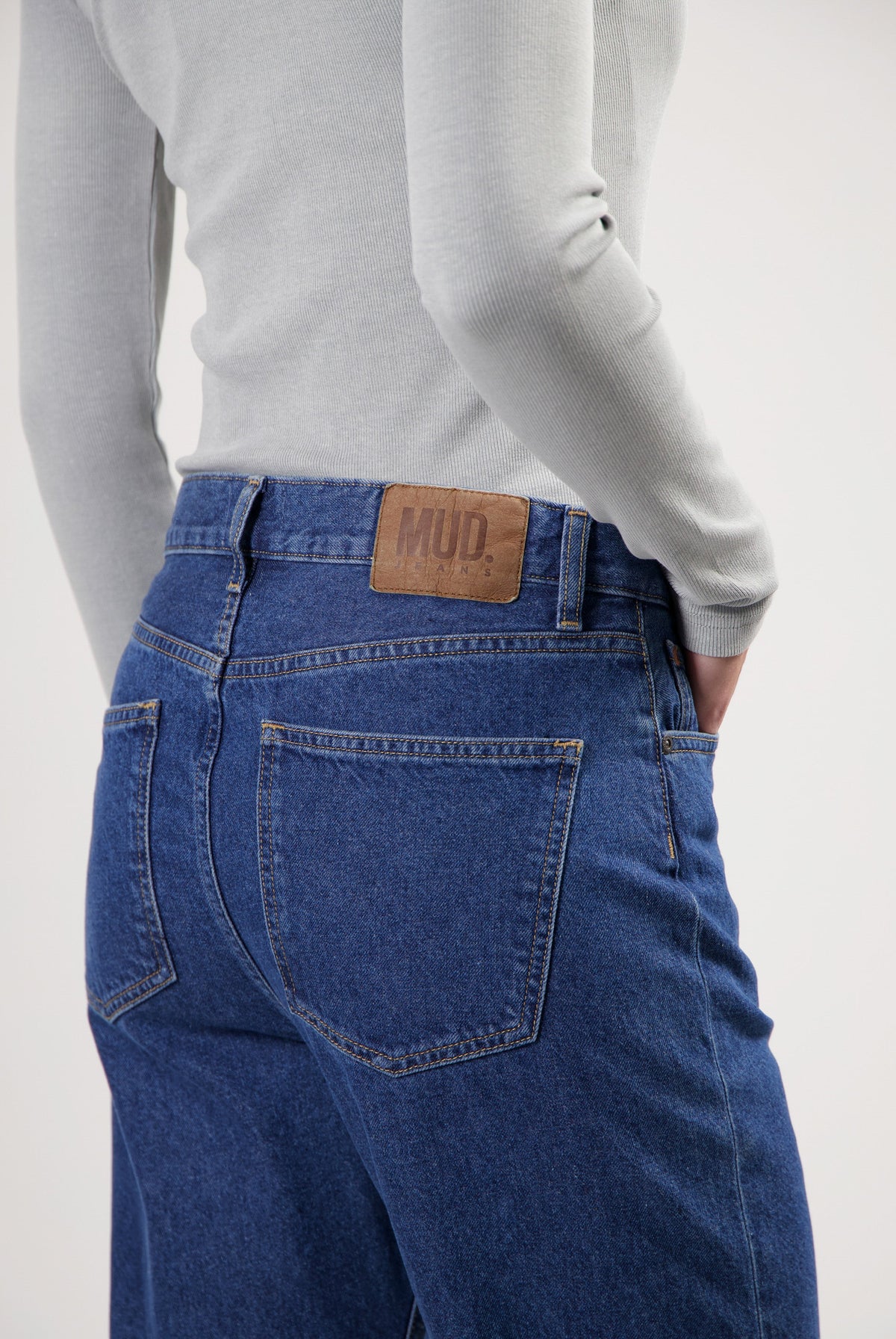 Gray long-sleeve top paired with eco-friendly dark blue MUD Jeans, highlighting back pockets and leather brand patch.