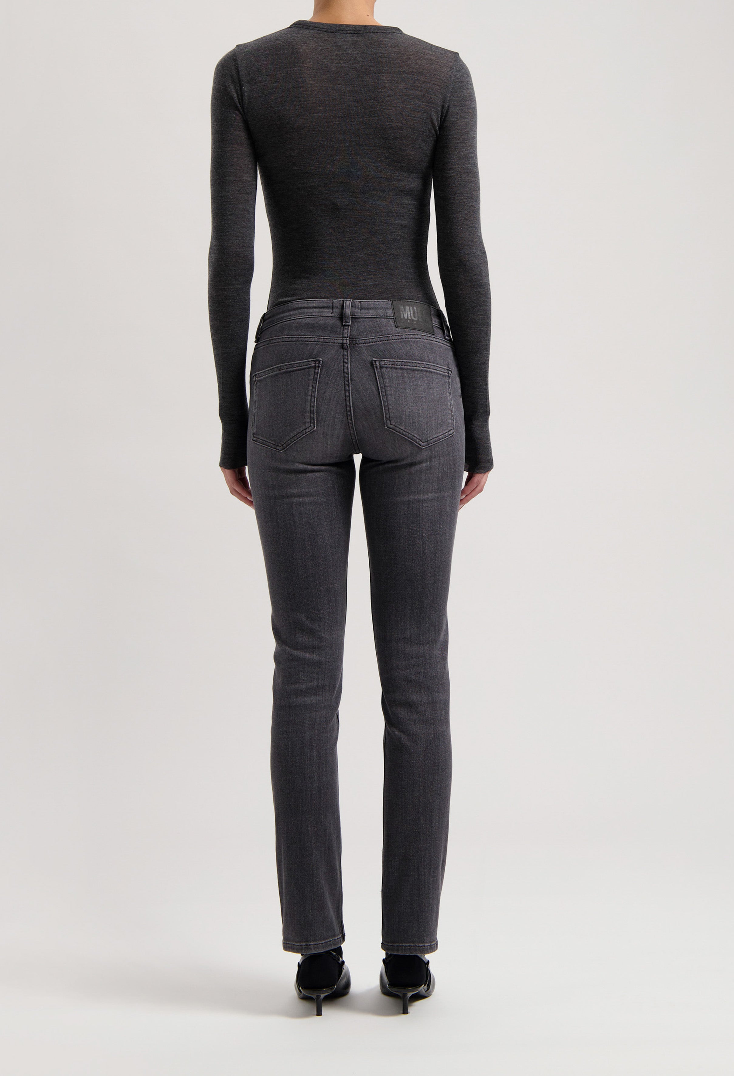 Back view of dark gray slim-fit denim jeans with a fitted long-sleeve charcoal top, highlighting sleek and modern fashion.