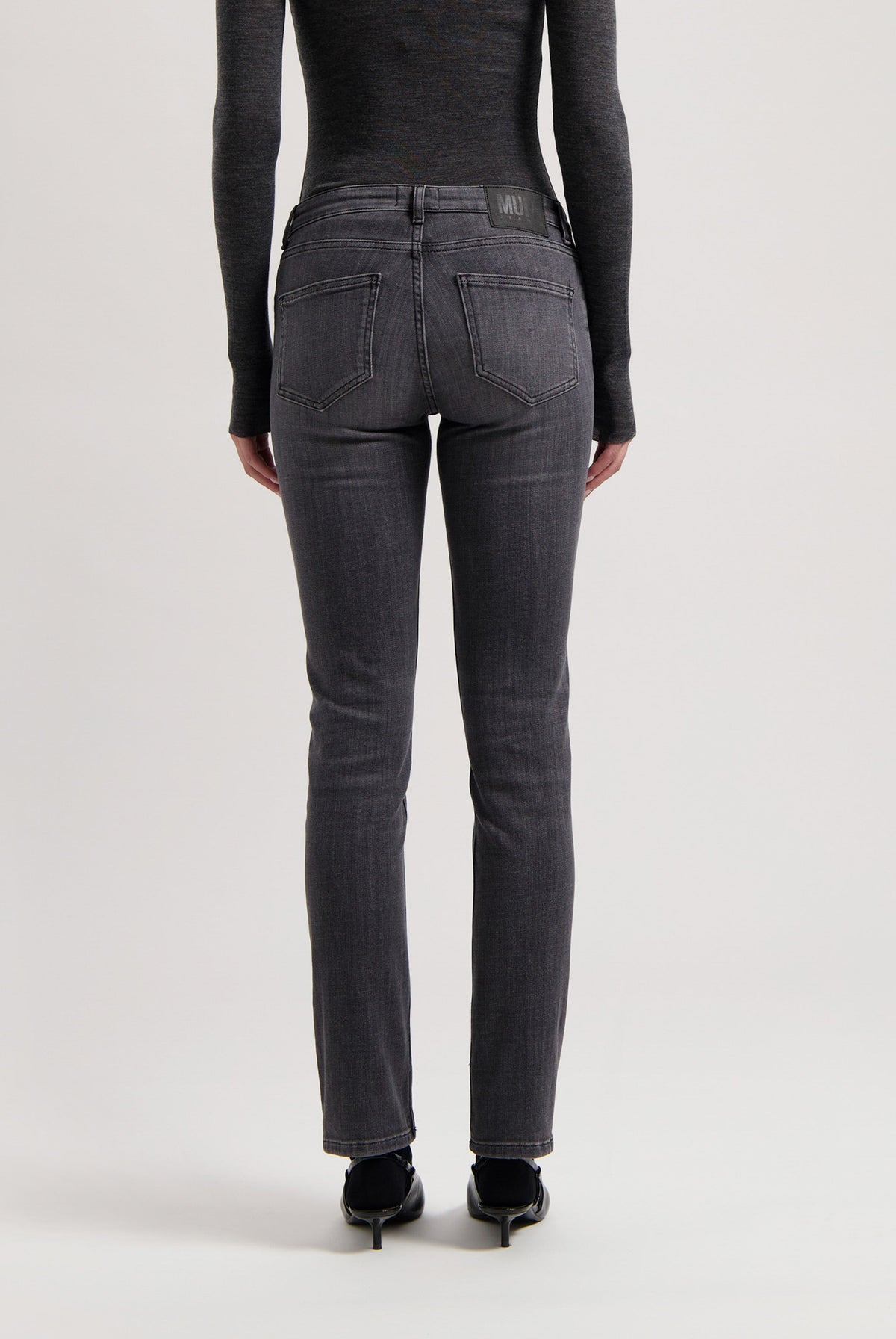 Dark gray, slim-fit MUD Jeans made from eco-friendly materials, showing a back view worn with a long-sleeve black top.