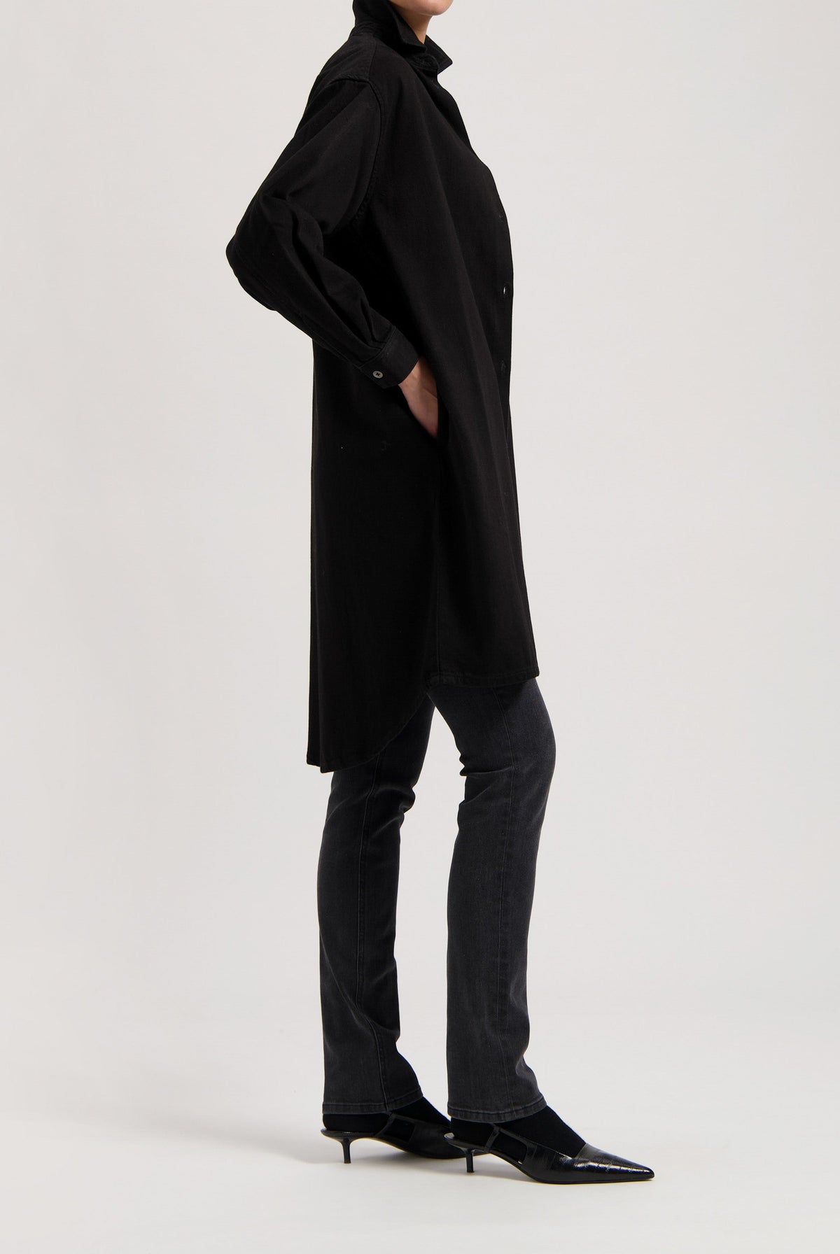 Black oversized shirt dress paired with dark gray, straight-leg jeans and pointed black kitten heels.