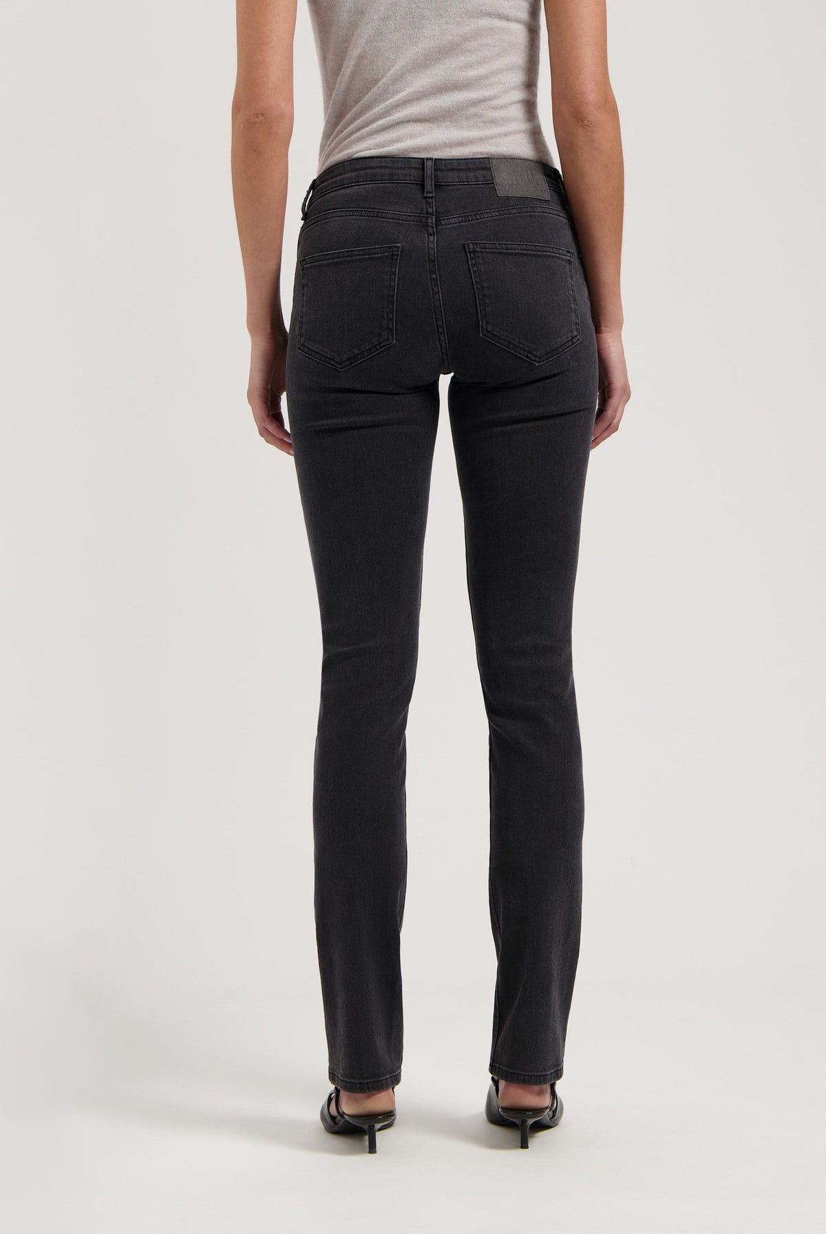 Dark gray slim-fit jeans on a model, highlighting the back pockets and straight leg cut, paired with a simple gray top.