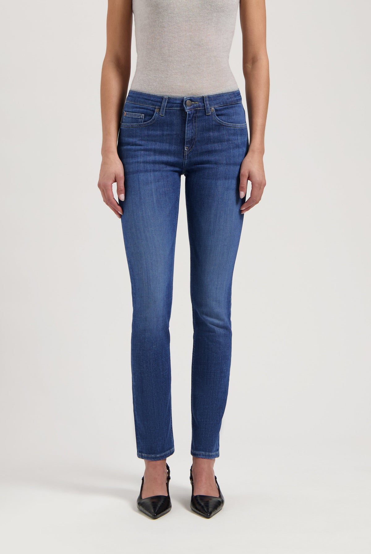 Woman wearing blue slim-fit jeans with a light gray sleeveless top, paired with black pointed heels.