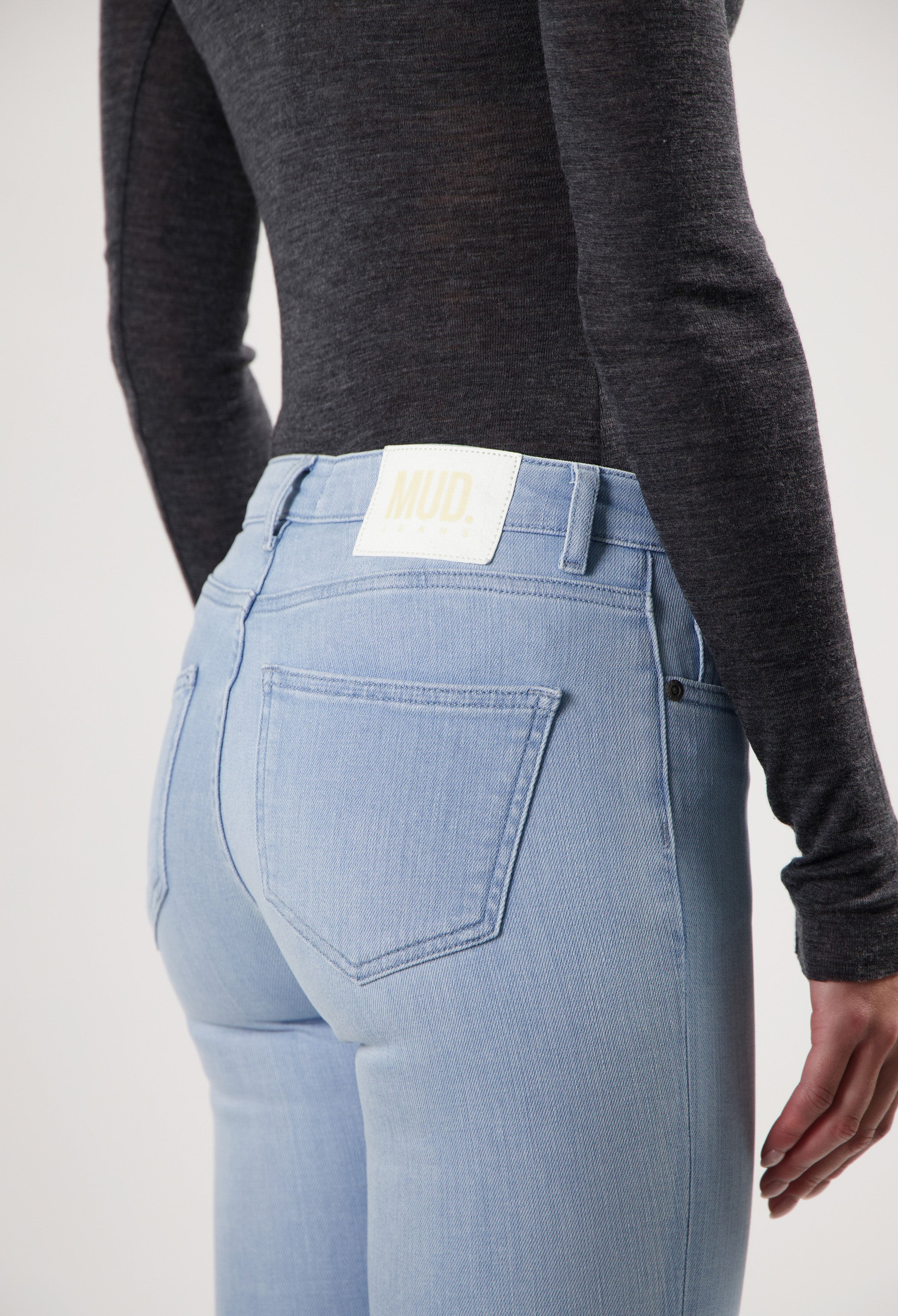Light blue, eco-friendly MUD Jeans made from organic cotton, featuring a back view with a black long-sleeve top.
