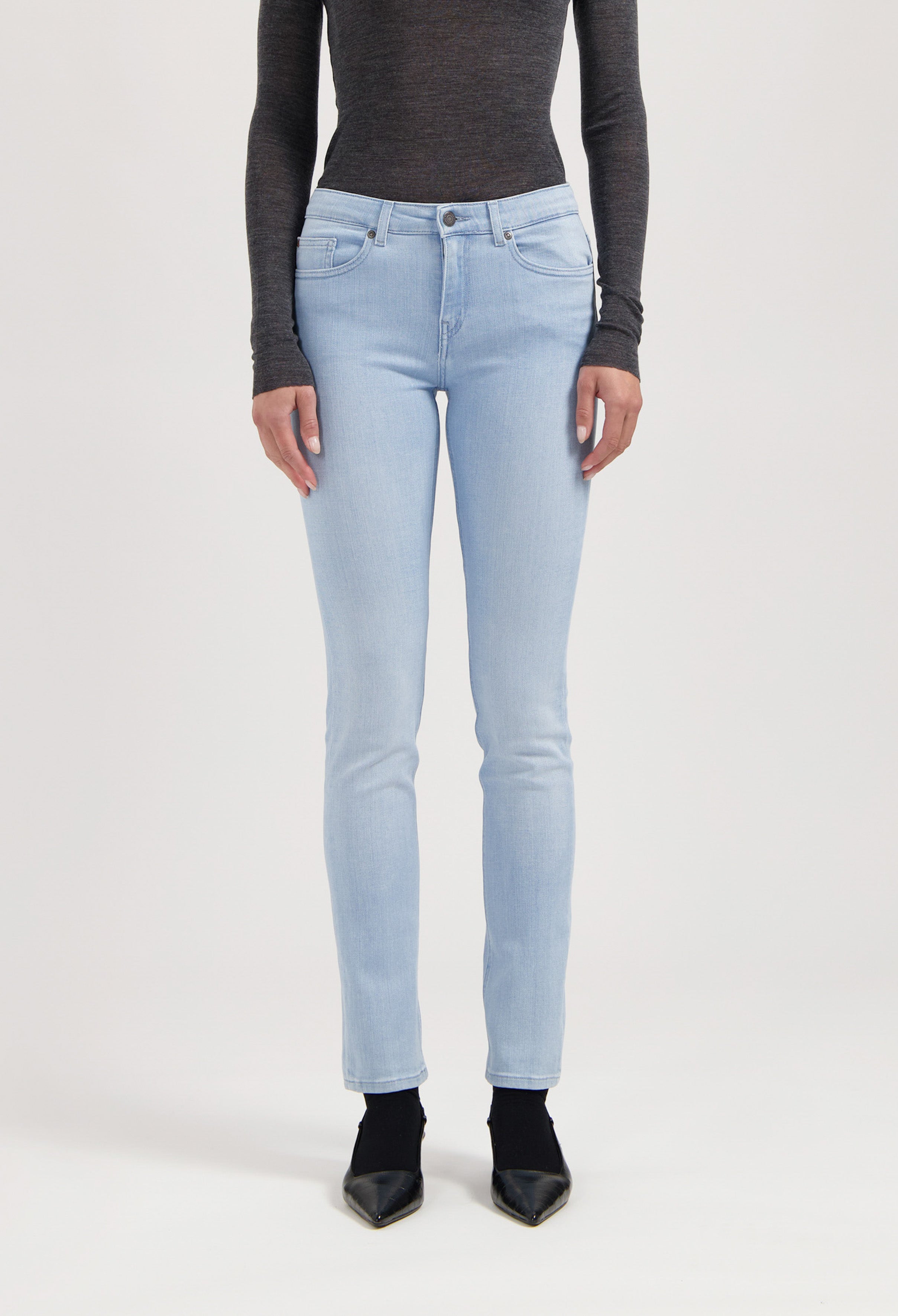Light blue stretch jeans in slim-fit style, coupled with a dark gray long-sleeve top and black pointed shoes.