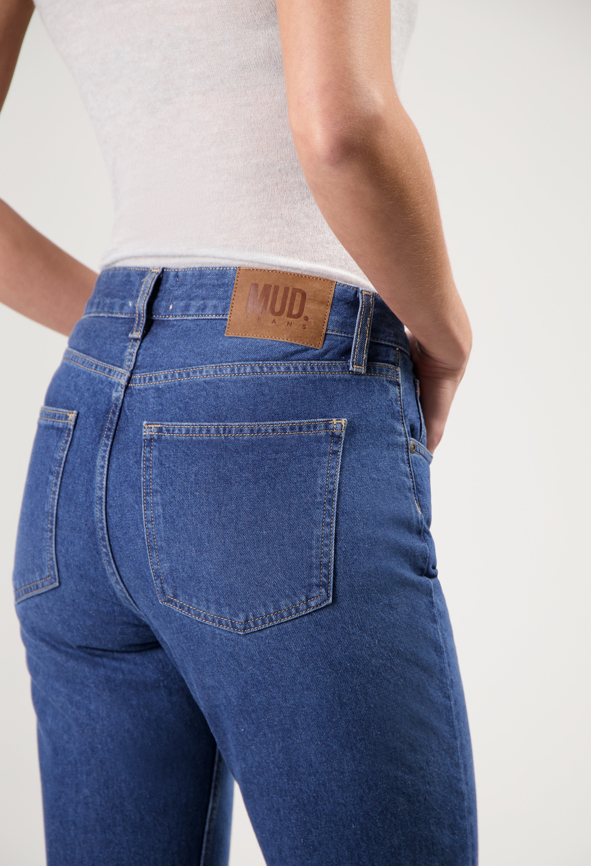 Dark blue MUD Jeans crafted from organic cotton, featuring back pocket stitching, worn with a white sleeveless top.