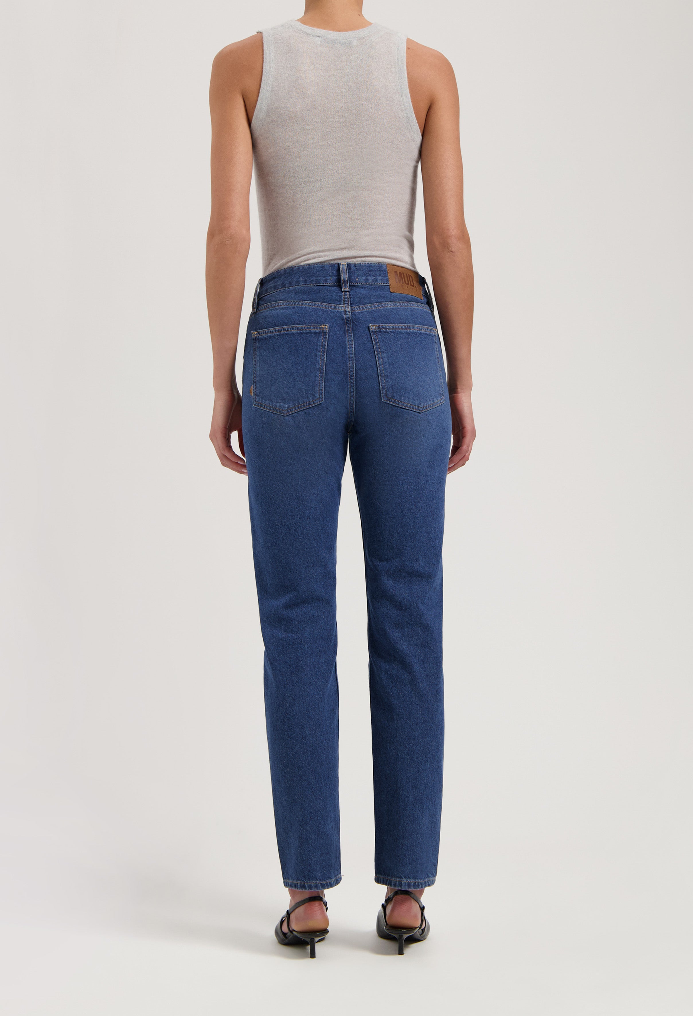 Person wearing sustainable dark blue denim jeans with a white sleeveless top, showcasing the back view and fit.
