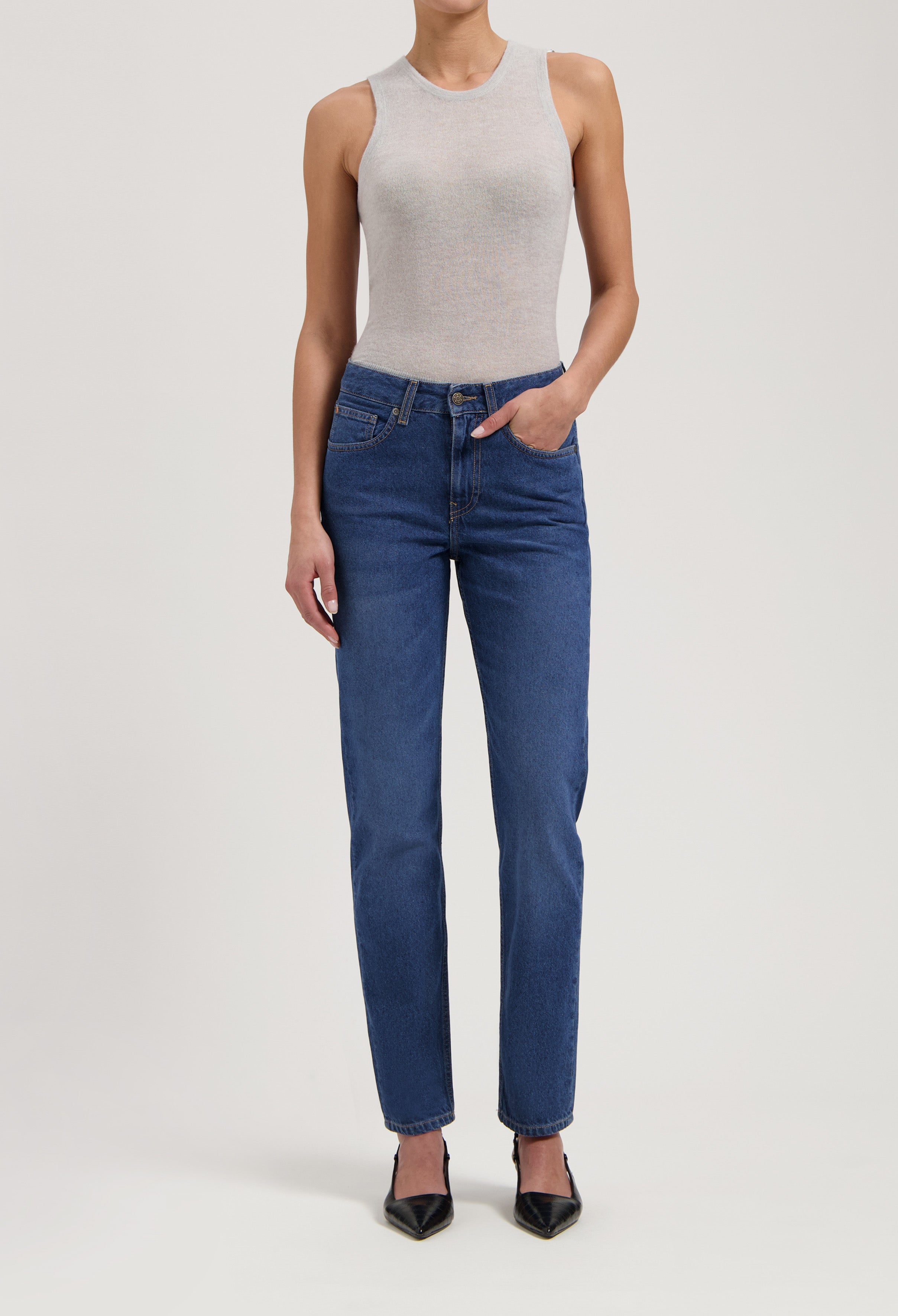 Model wearing a sleeveless gray top paired with classic blue high-waisted jeans and black pointed heels.