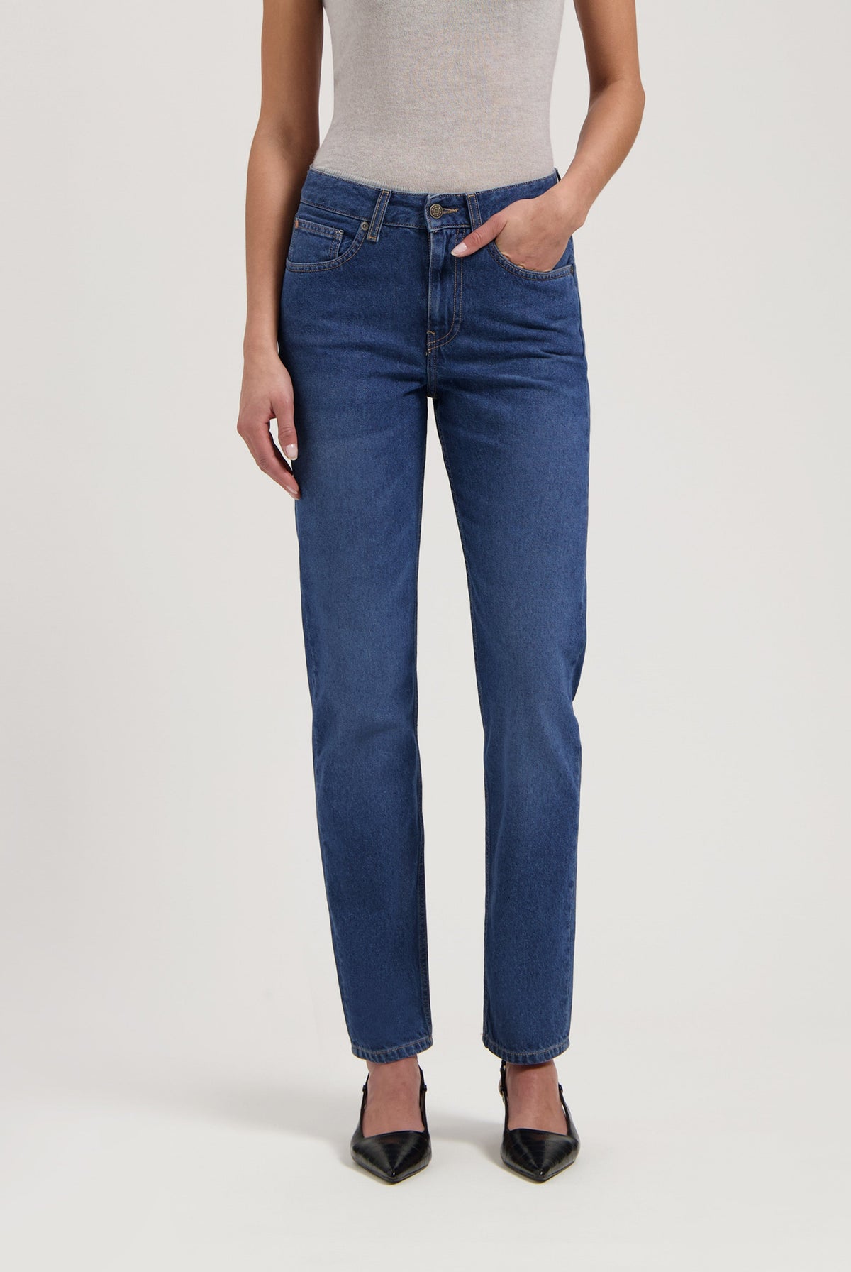 Stylish blue straight-leg jeans paired with a light gray sleeveless top and black pointed-toe heels.