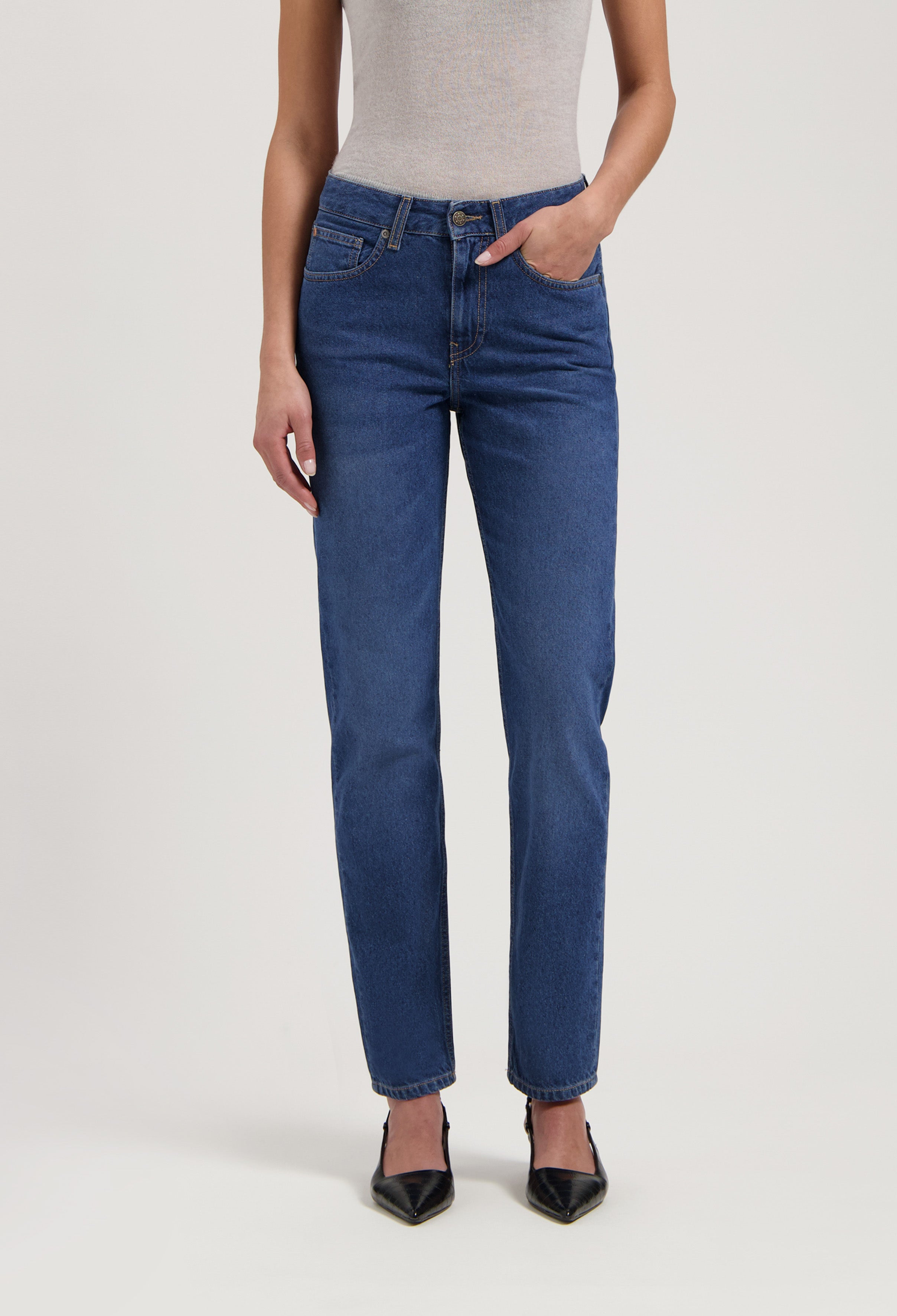 Stylish blue straight-leg jeans paired with a light gray sleeveless top and black pointed-toe heels.