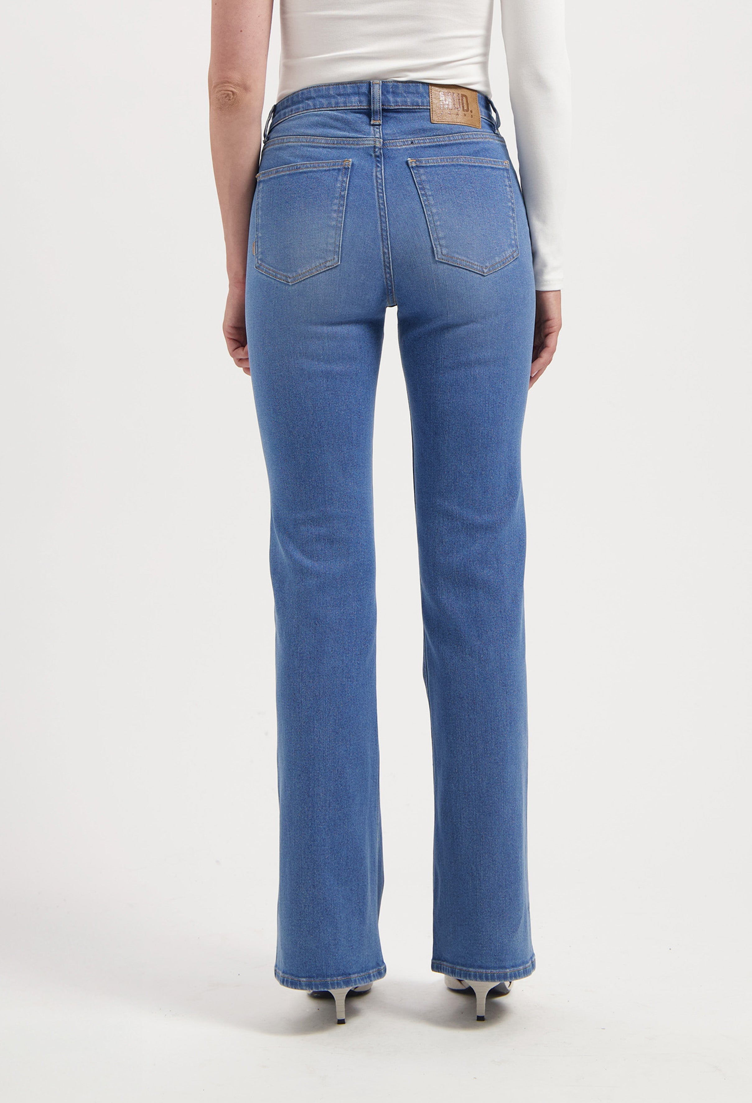 Back view of blue MUD Jeans made from organic cotton, featuring a high-waisted, straight-leg fit worn with a white long-sleeve top.