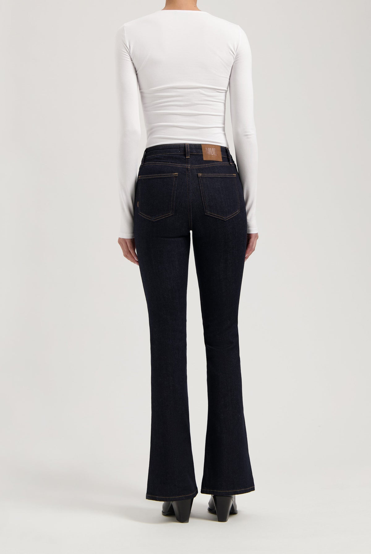 Dark blue flared denim jeans paired with a form-fitting white long sleeve top, highlighting a modern casual style.