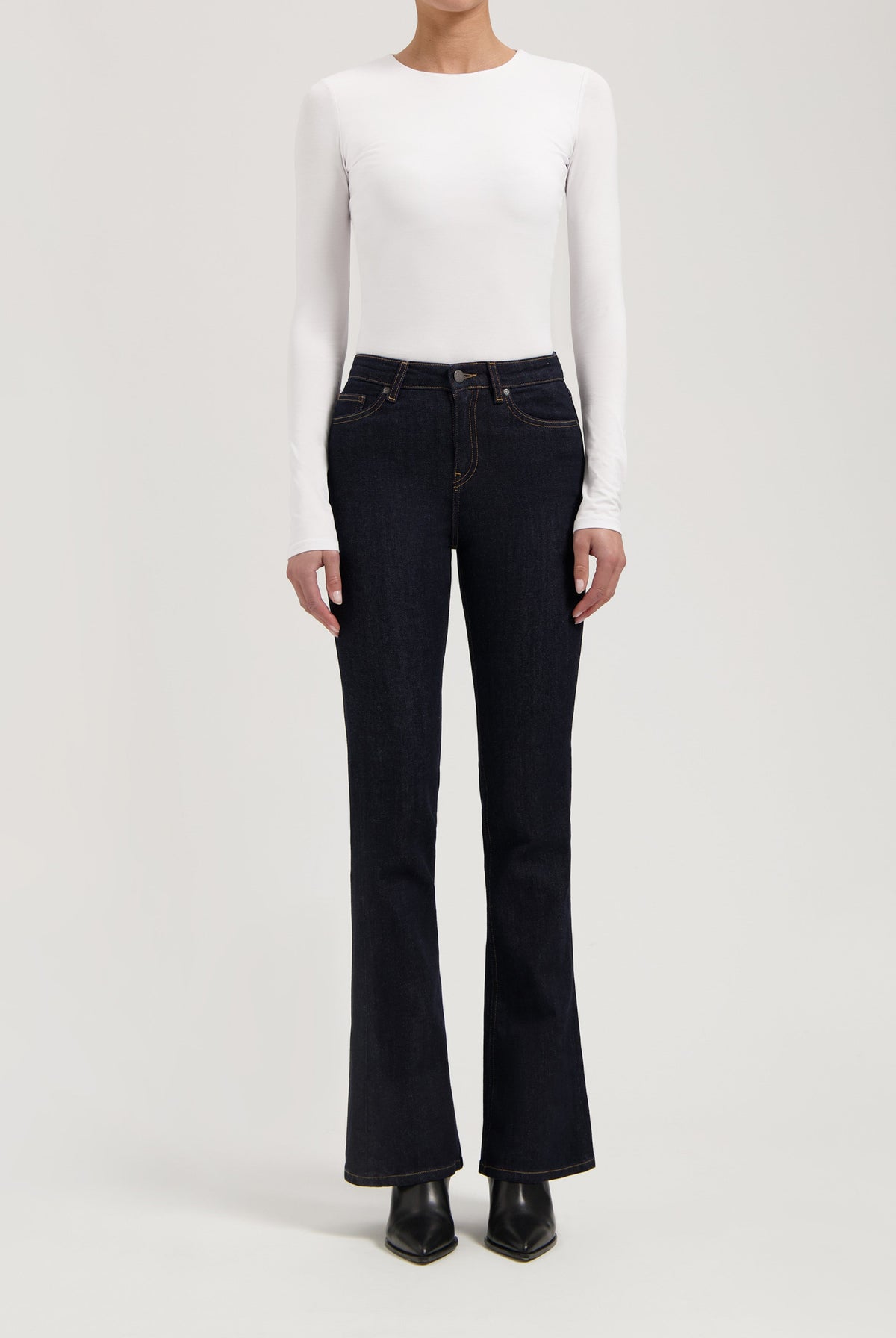 Woman wearing dark blue bootcut jeans with a white long-sleeve fitted top, showcasing casual chic style.