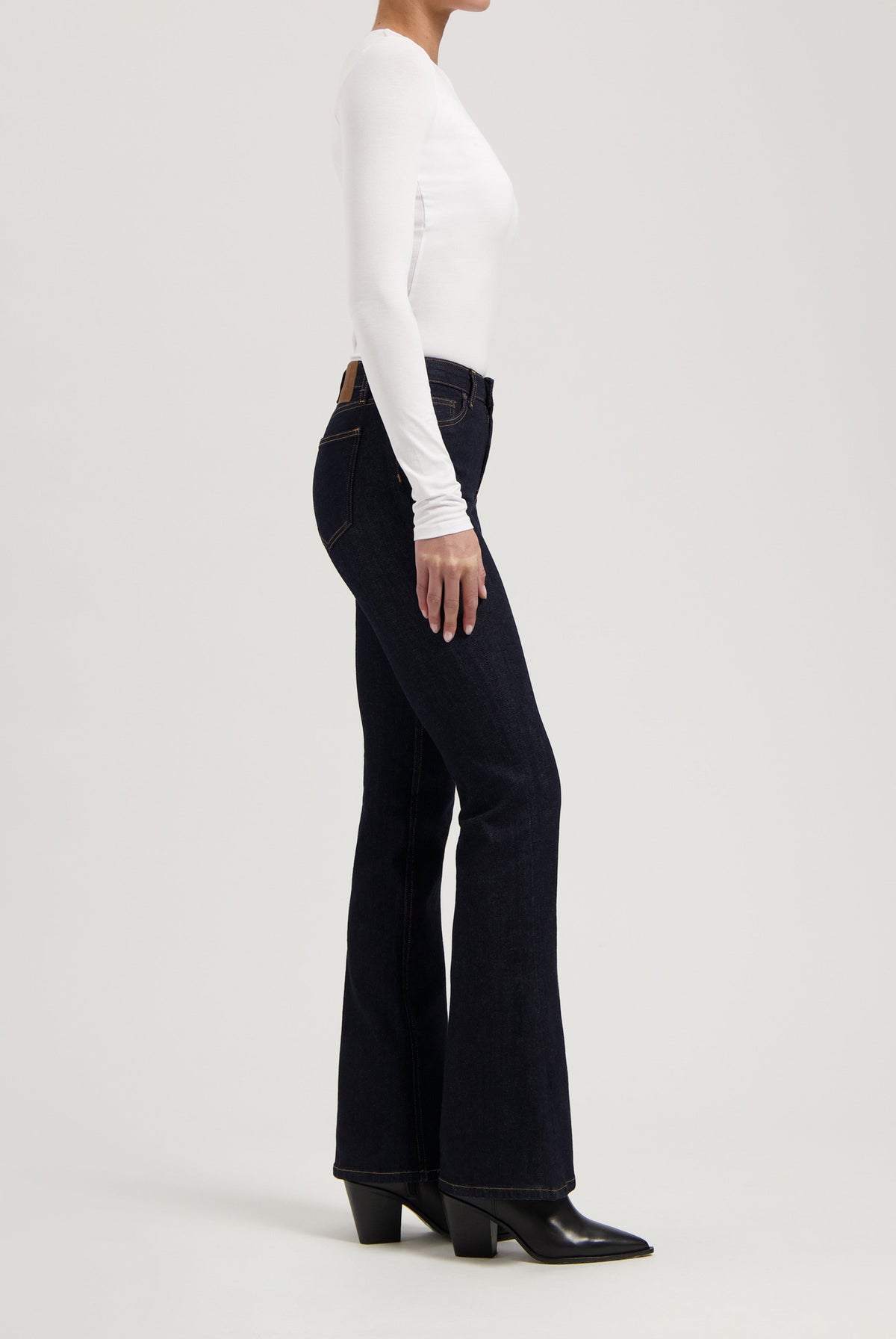 Model wearing dark blue flare jeans paired with a fitted white long-sleeve top and black heeled ankle boots.
