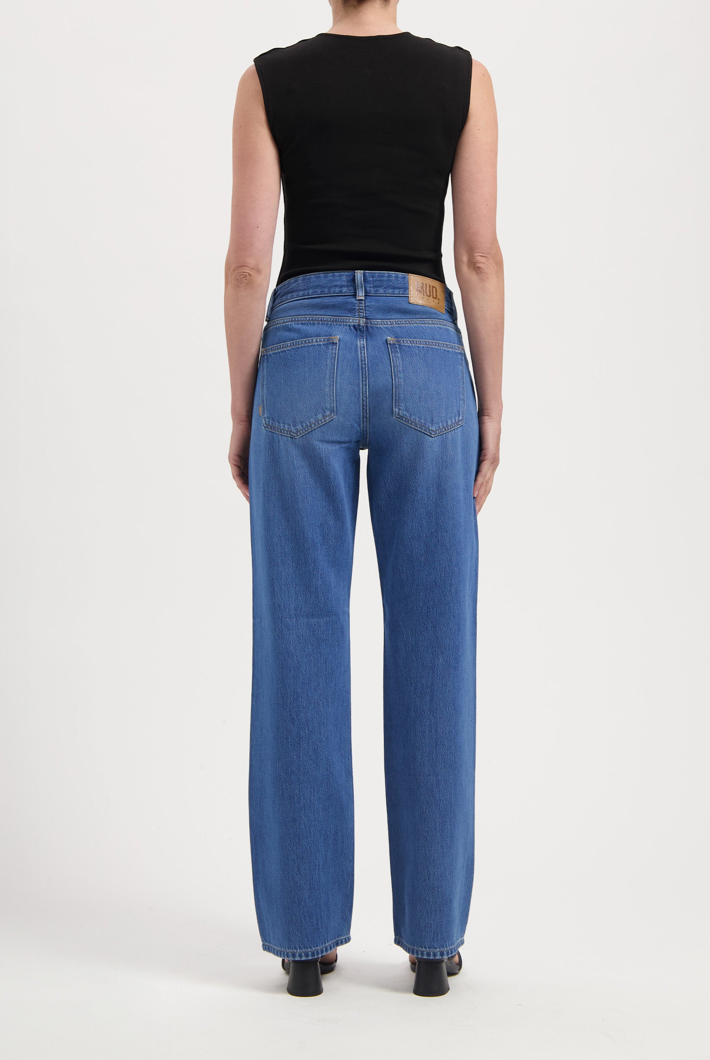 Back view of person wearing classic MUD Jeans in medium blue, wide-leg style, paired with a sleeveless black top.