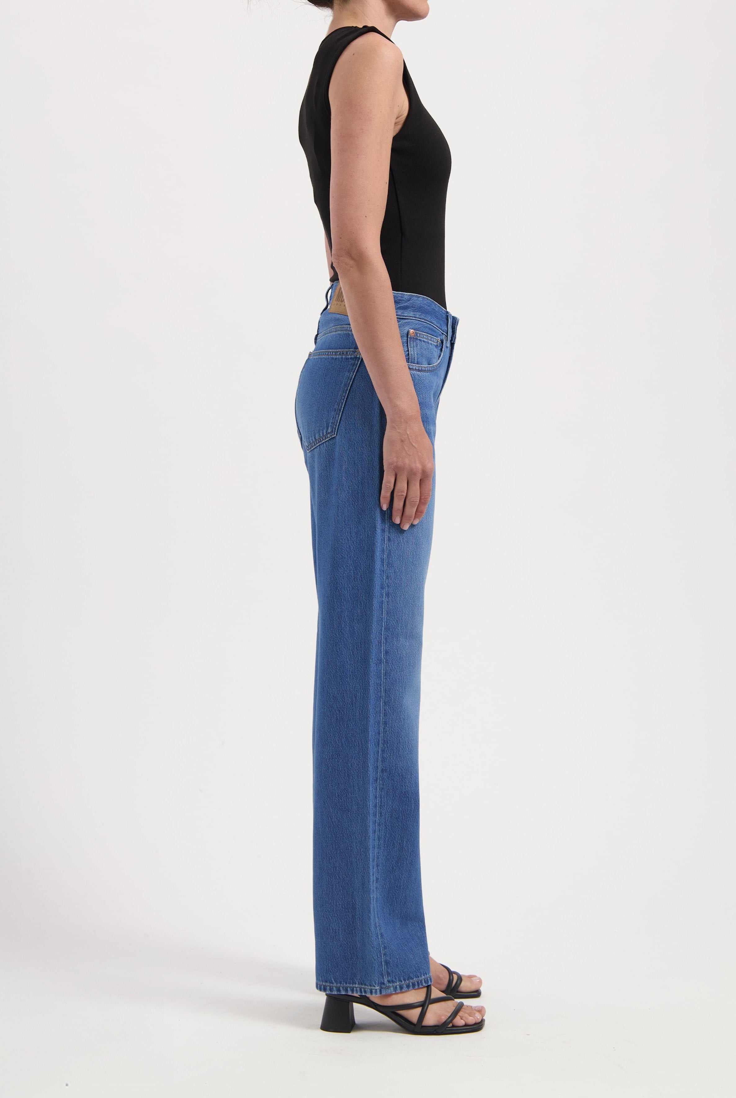 Woman wearing fitted blue jeans and a sleeveless black top, showcasing casual style with strappy black heels.