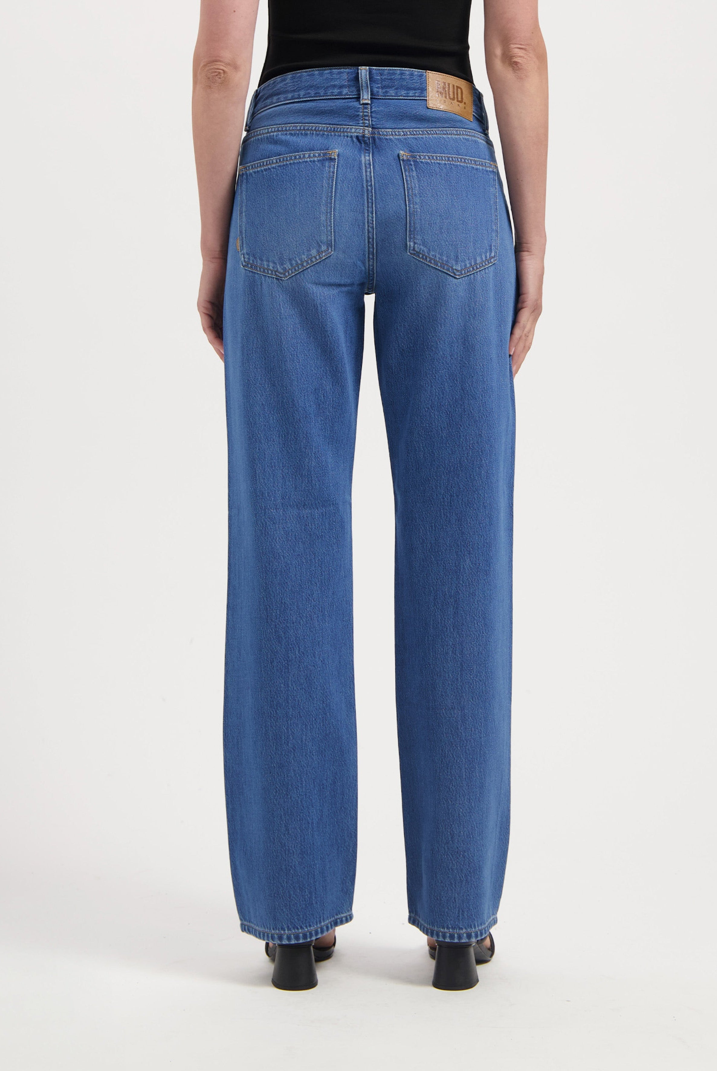 Back view of sustainable wide-leg jeans in indigo, styled with a simple black sleeveless top and black heeled shoes.