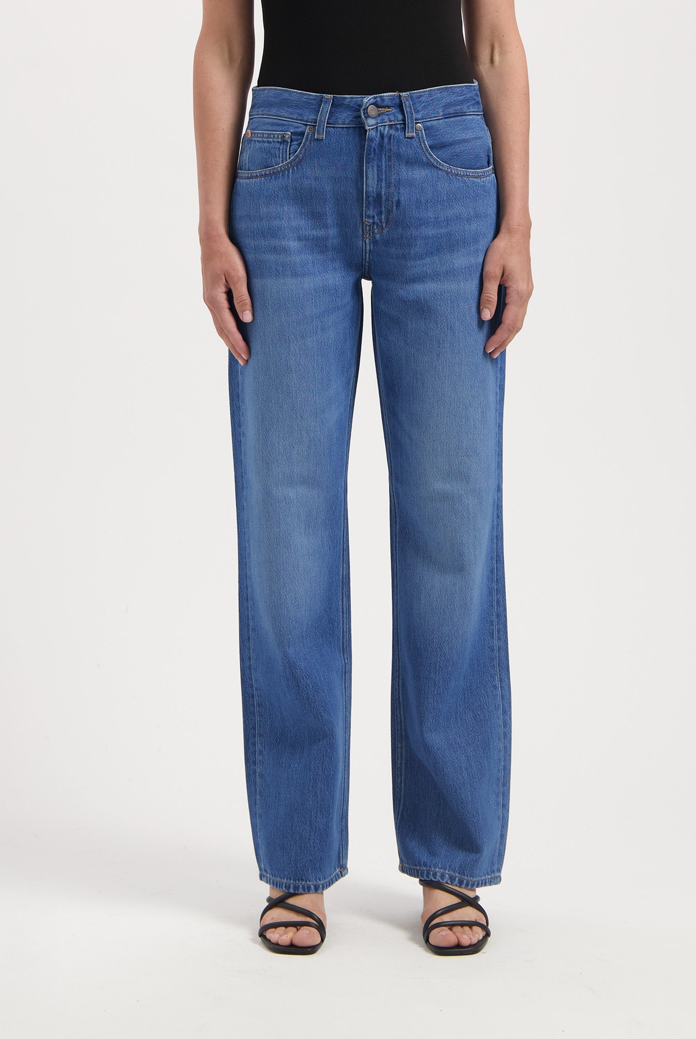 High-rise wide-leg jeans in classic blue denim, featuring a subtle fade, worn with a simple black top and strappy sandals.