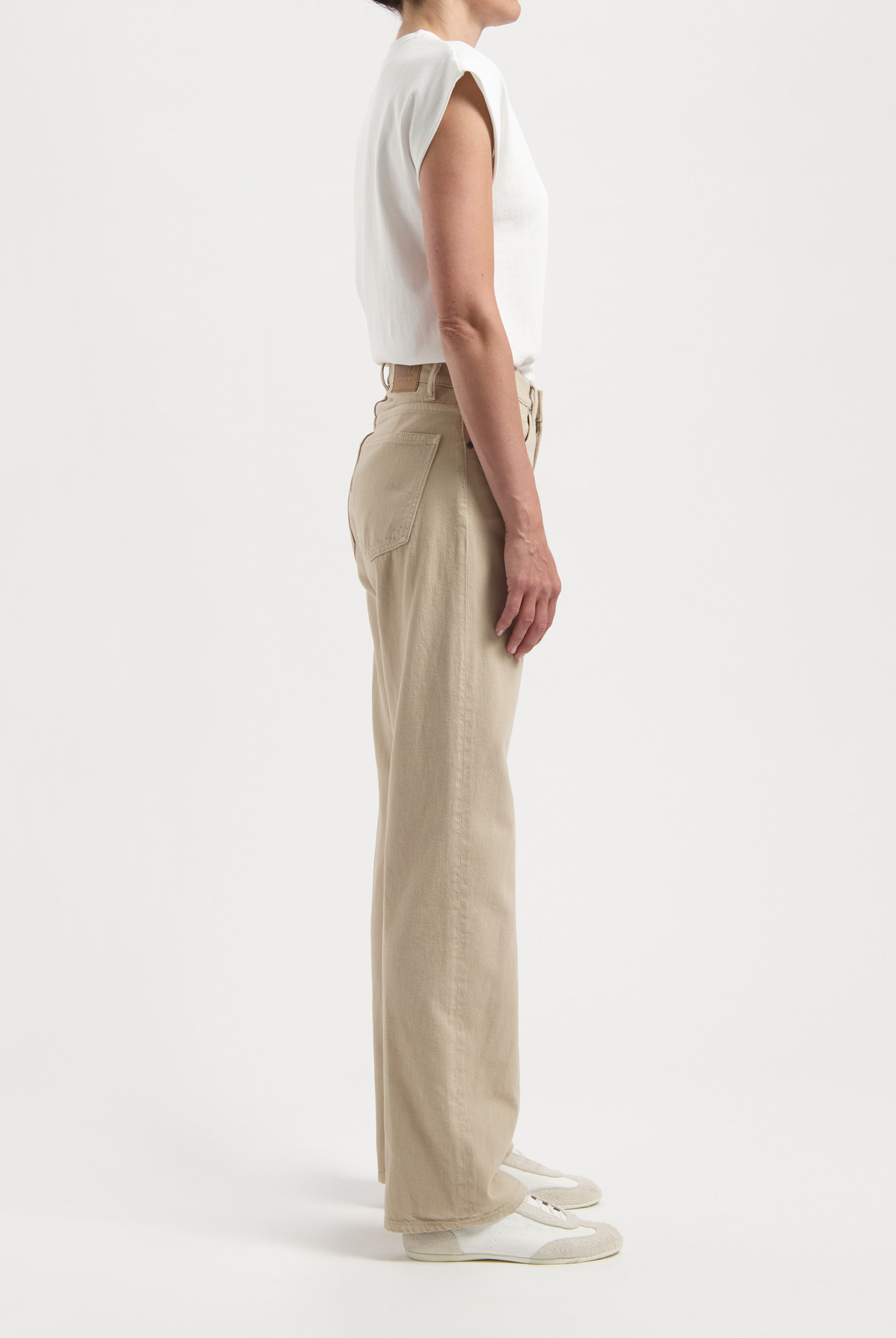 Side profile of a person wearing beige high-waisted, straight-leg cotton pants paired with a white sleeveless top.