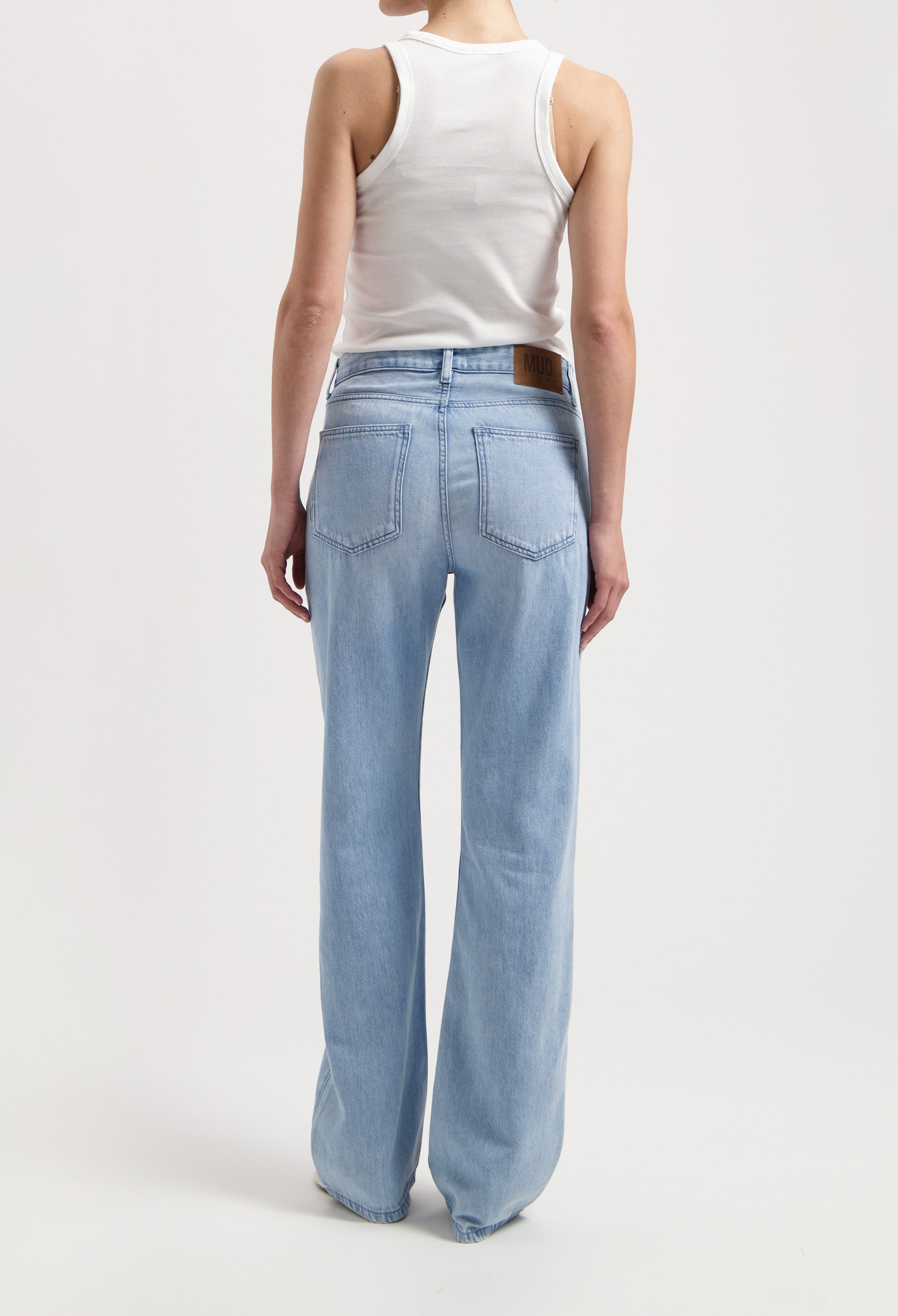 Back view of light blue wide-leg MUD Jeans with high waist, paired with a fitted white tank top, showcasing the sustainable denim design.