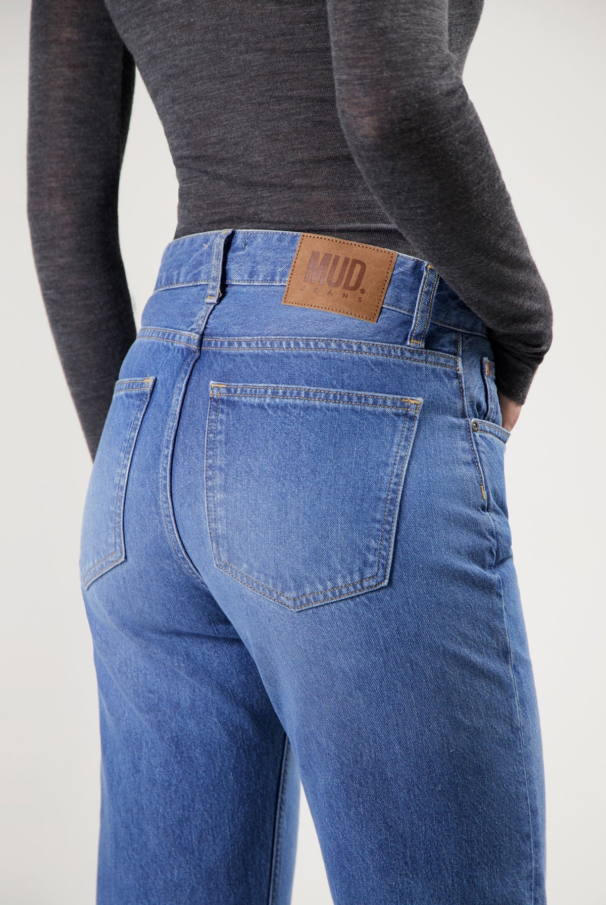 Back view of sustainable MUD Jeans in blue denim, high-waisted fit, paired with a dark gray long-sleeve top.