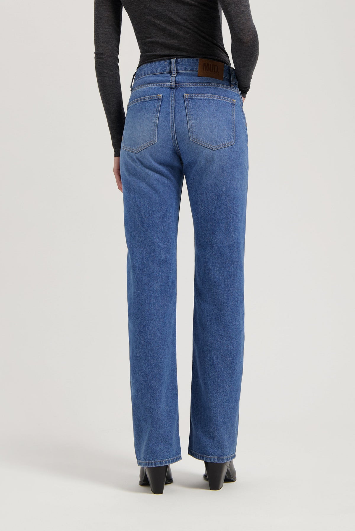 Rear view of classic straight-leg blue MUD Jeans made from organic cotton, paired with a fitted dark gray long-sleeve top.
