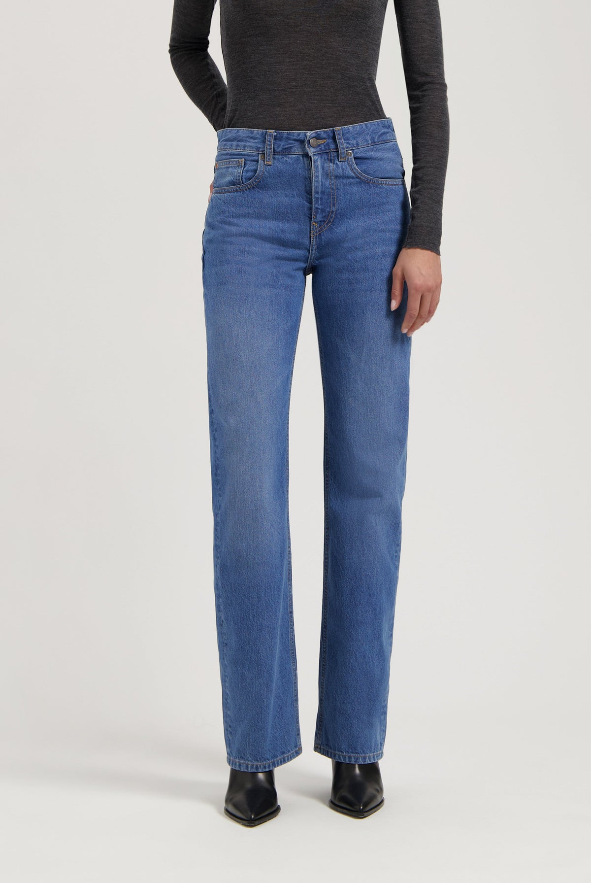 Model wearing mid-rise blue denim jeans with a straight-leg fit, paired with a dark gray long-sleeve top and black boots.