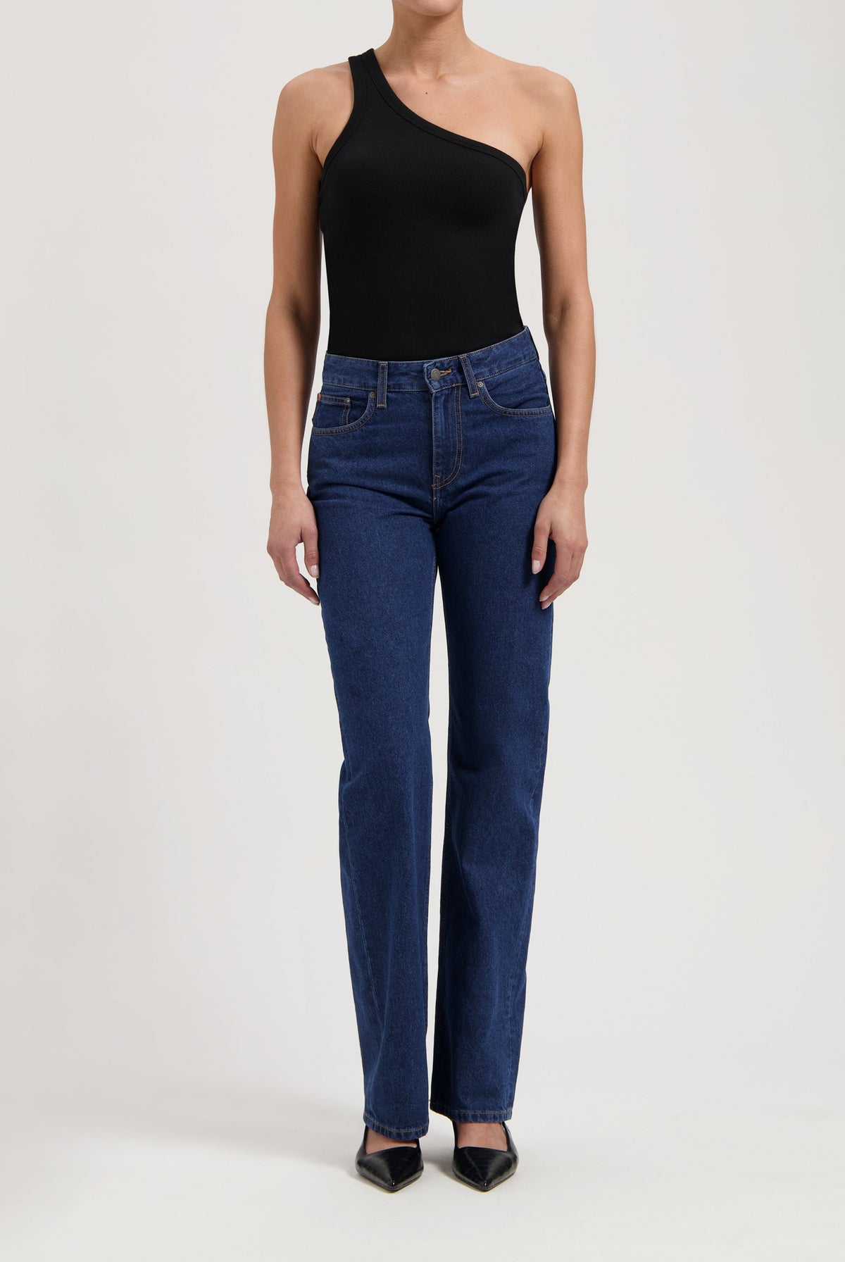 One-shoulder black bodysuit styled with classic dark blue high-waisted jeans and black pointed-toe heels.