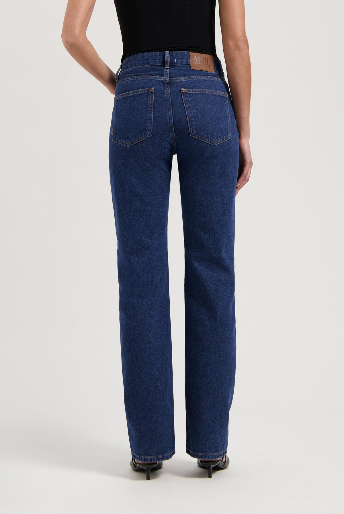 High-waisted, eco-friendly deep blue women's jeans showcasing straight-leg fit, paired with a black sleeveless top.