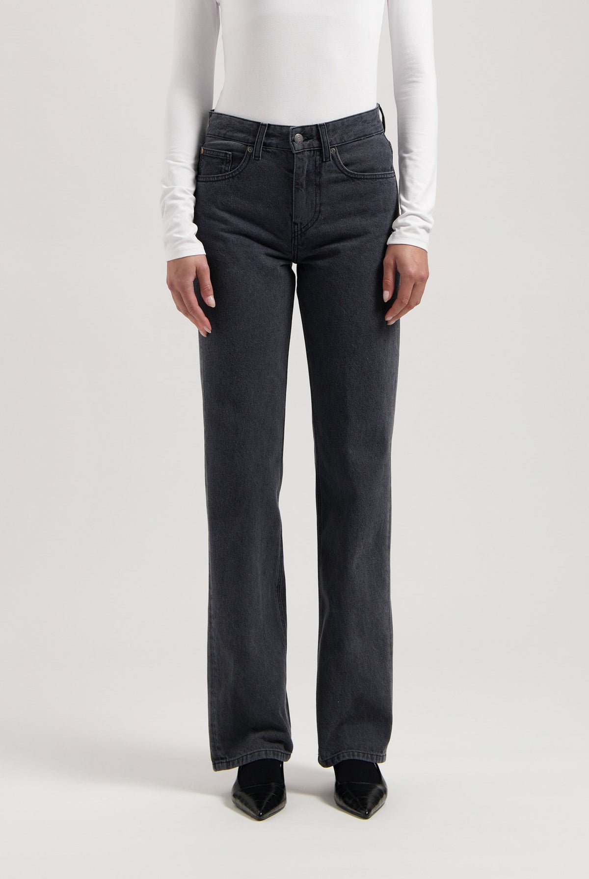 Straight-leg black denim jeans paired with a fitted white long-sleeve top, showcasing a minimalist style.