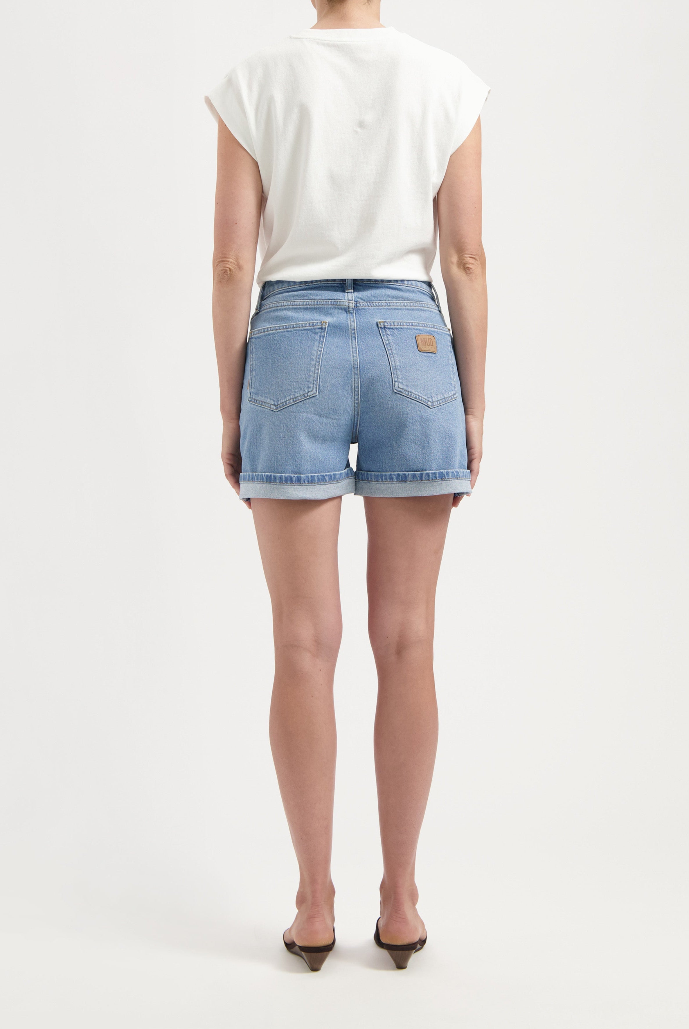Back view of light blue denim shorts with rolled hems paired with a sleeveless white top, showcasing casual summer fashion.