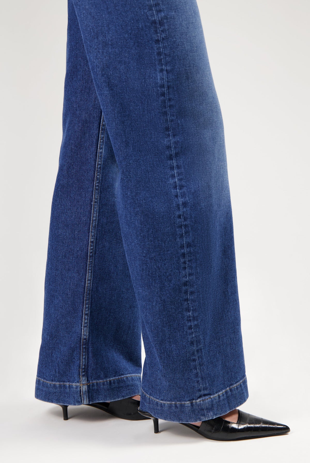 Wide-leg indigo denim jeans in a deep blue shade, paired with sleek black pointed-toe heels, show modern casual style.