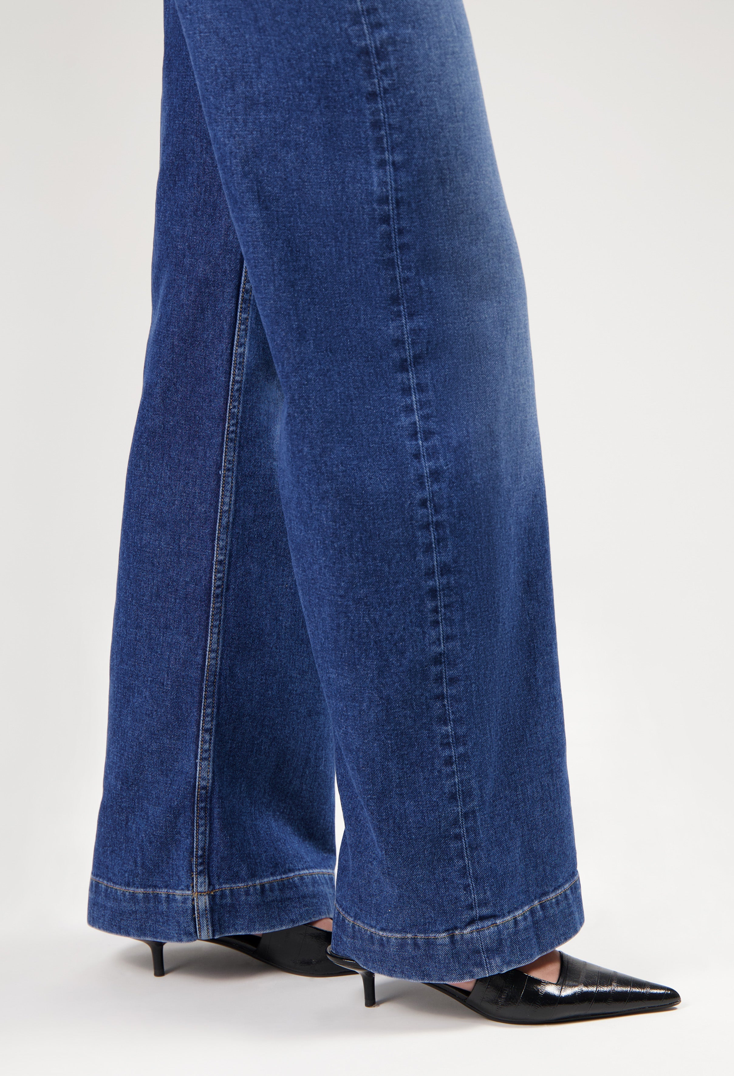 Wide-leg indigo denim jeans in a deep blue shade, paired with sleek black pointed-toe heels, show modern casual style.