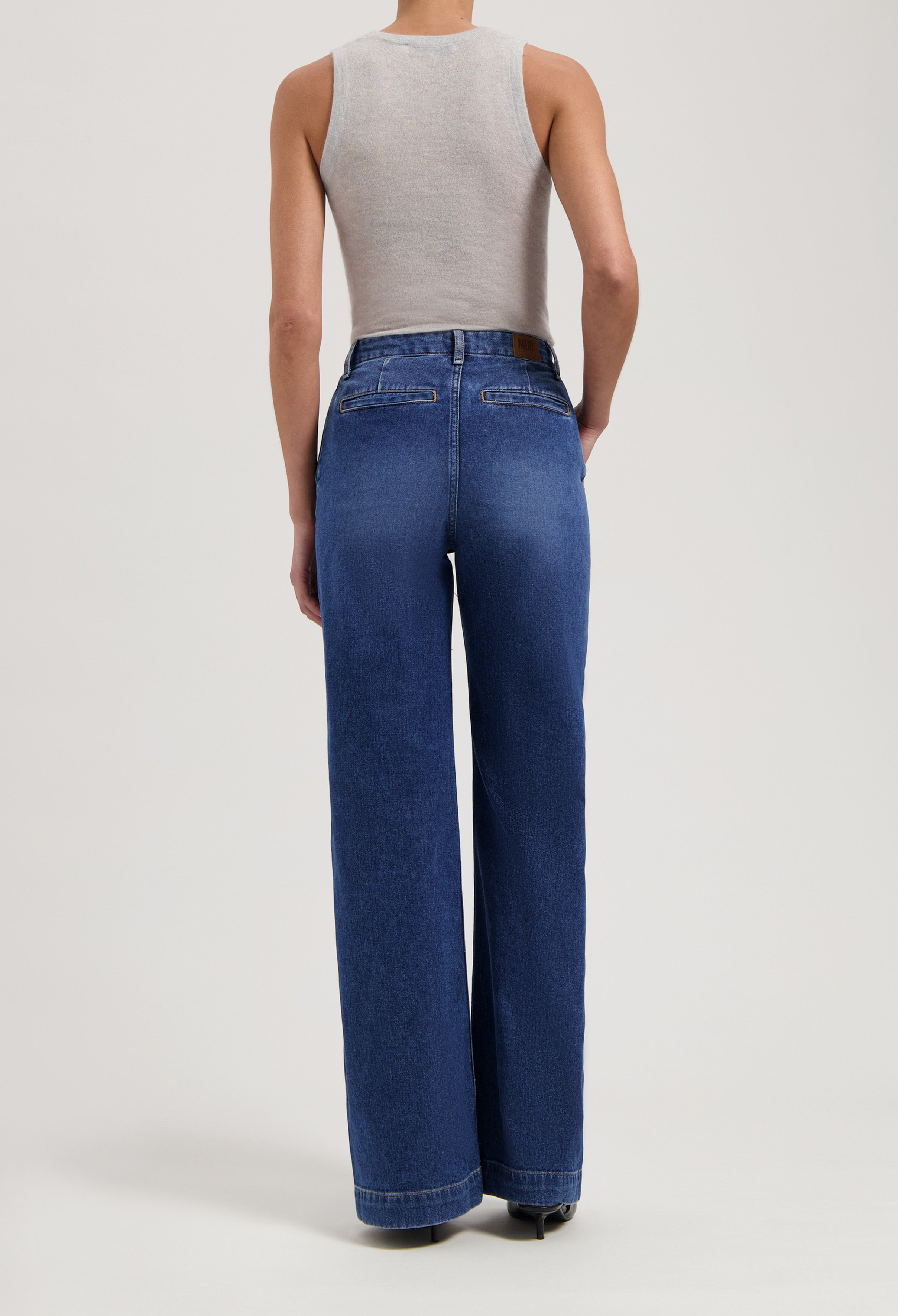 Rear view of model in blue high-waisted, wide-leg denim jeans paired with a sleeveless light gray top.