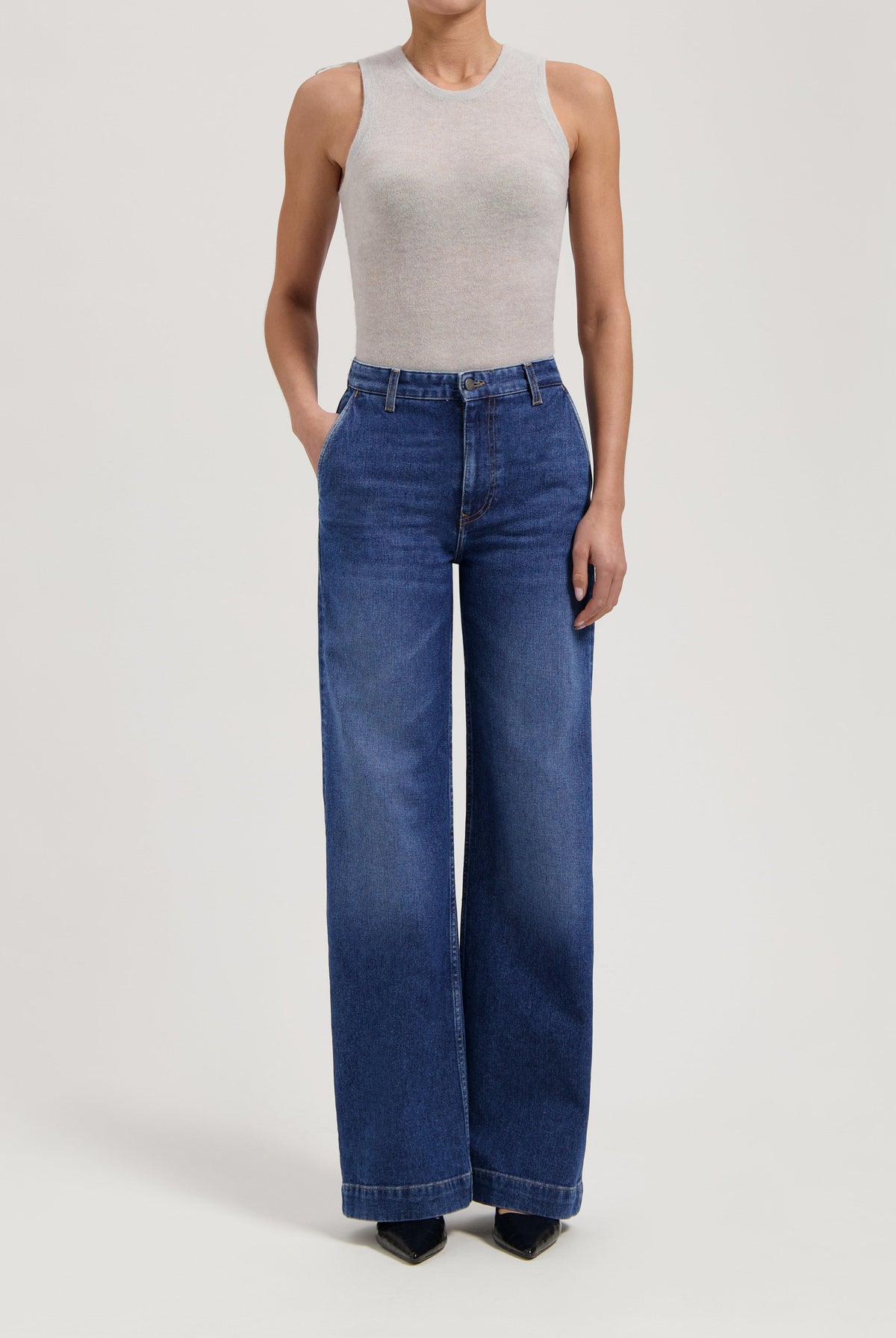 Woman wearing wide-leg blue denim jeans paired with a sleeveless light gray top in a minimalist style.