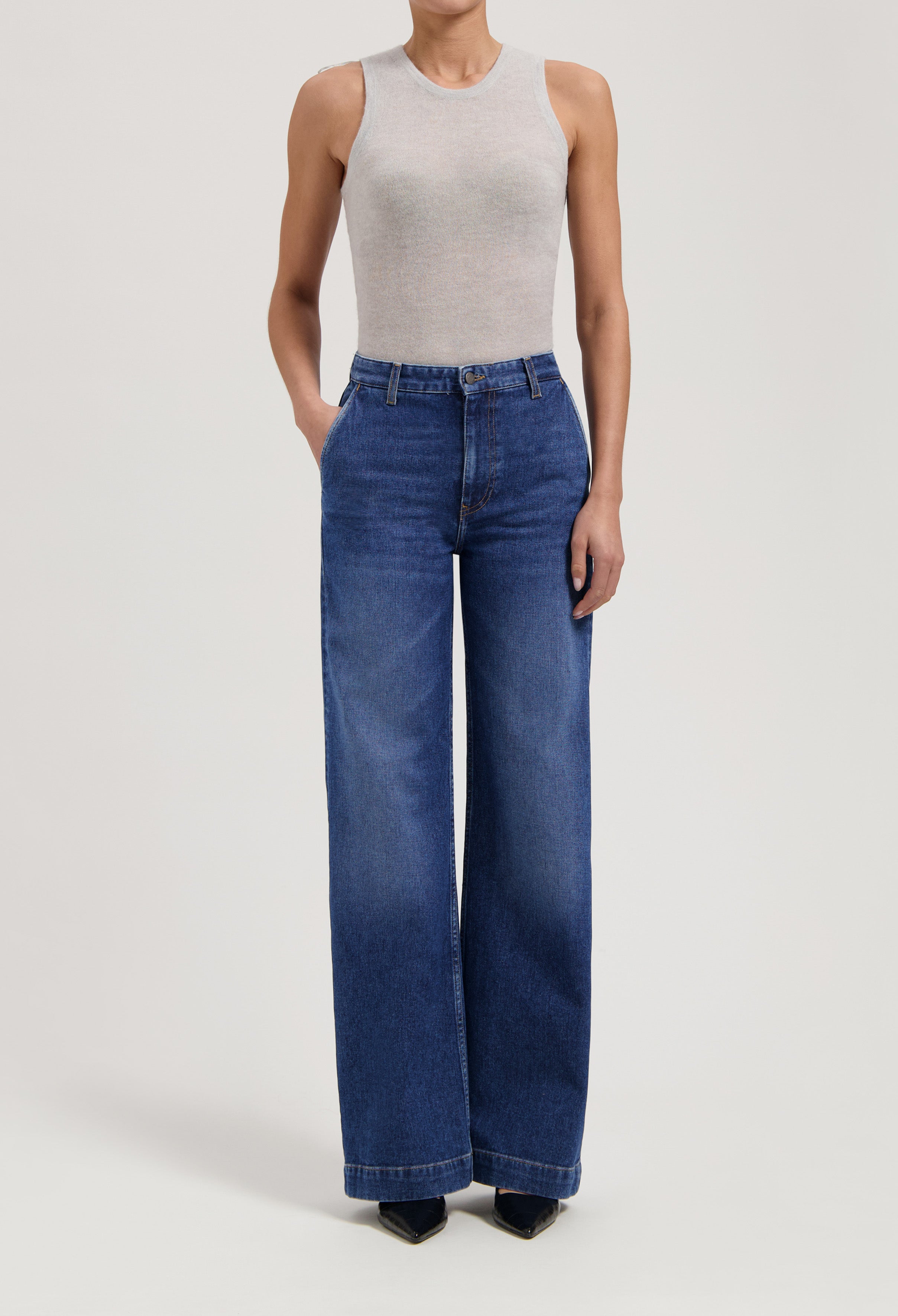 Woman wearing wide-leg blue denim jeans paired with a sleeveless light gray top in a minimalist style.
