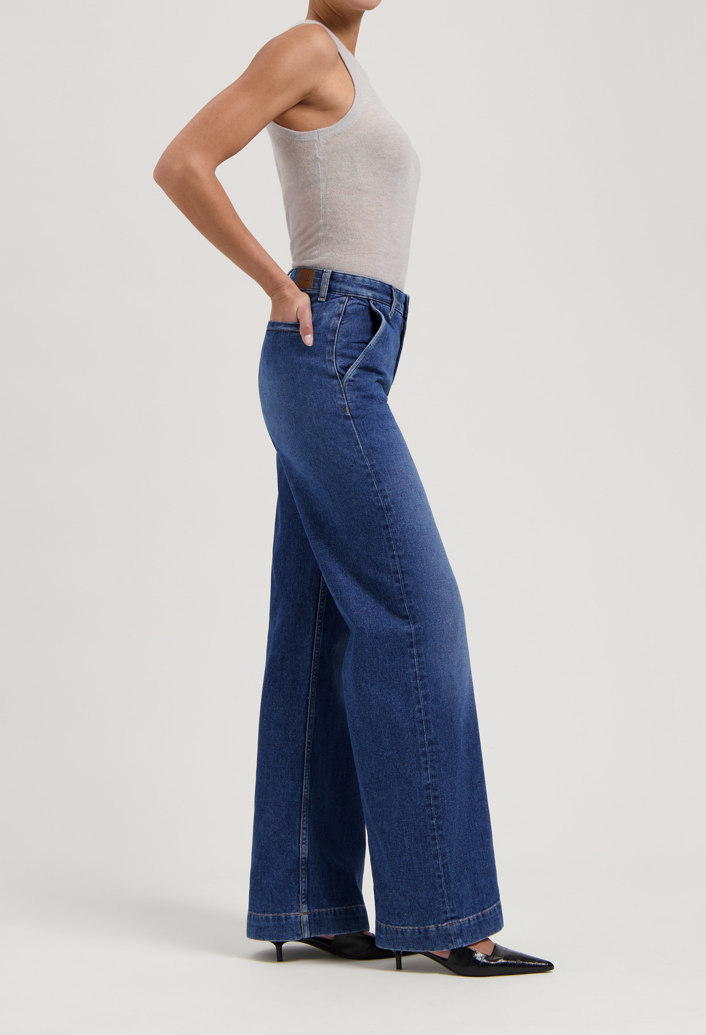 Wide-leg denim jeans in deep blue, paired with a sleeveless gray top, highlighted on a woman wearing black heels.