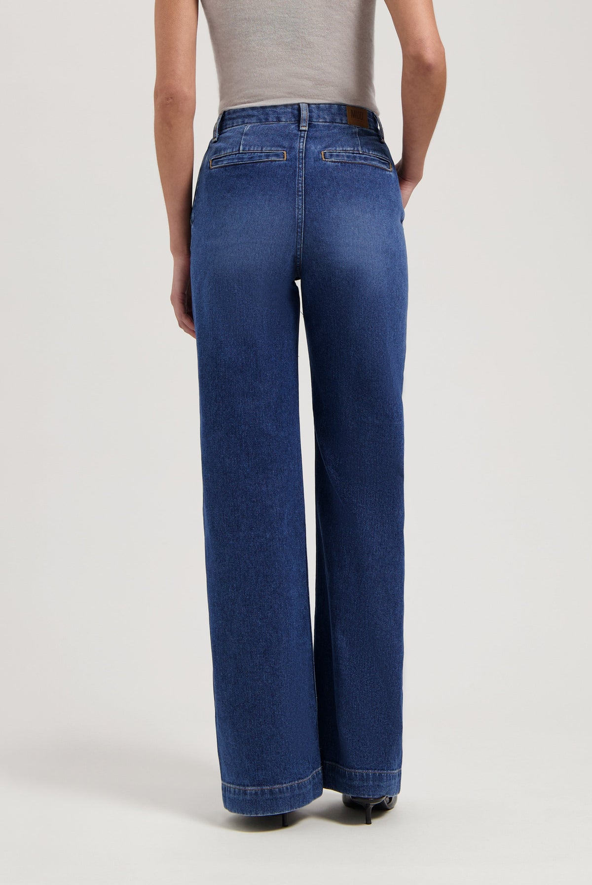 Wide-leg blue denim jeans worn with a sleeveless gray top, highlighting relaxed fit and mid-rise waist in a studio setting.