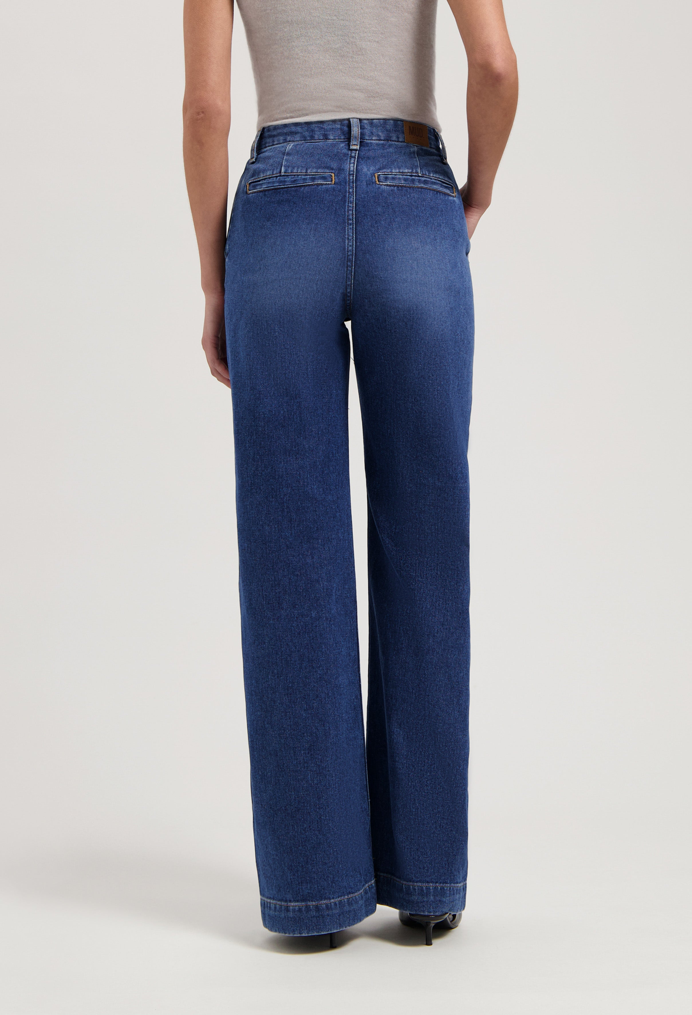 Wide-leg blue denim jeans worn with a sleeveless gray top, highlighting relaxed fit and mid-rise waist in a studio setting.